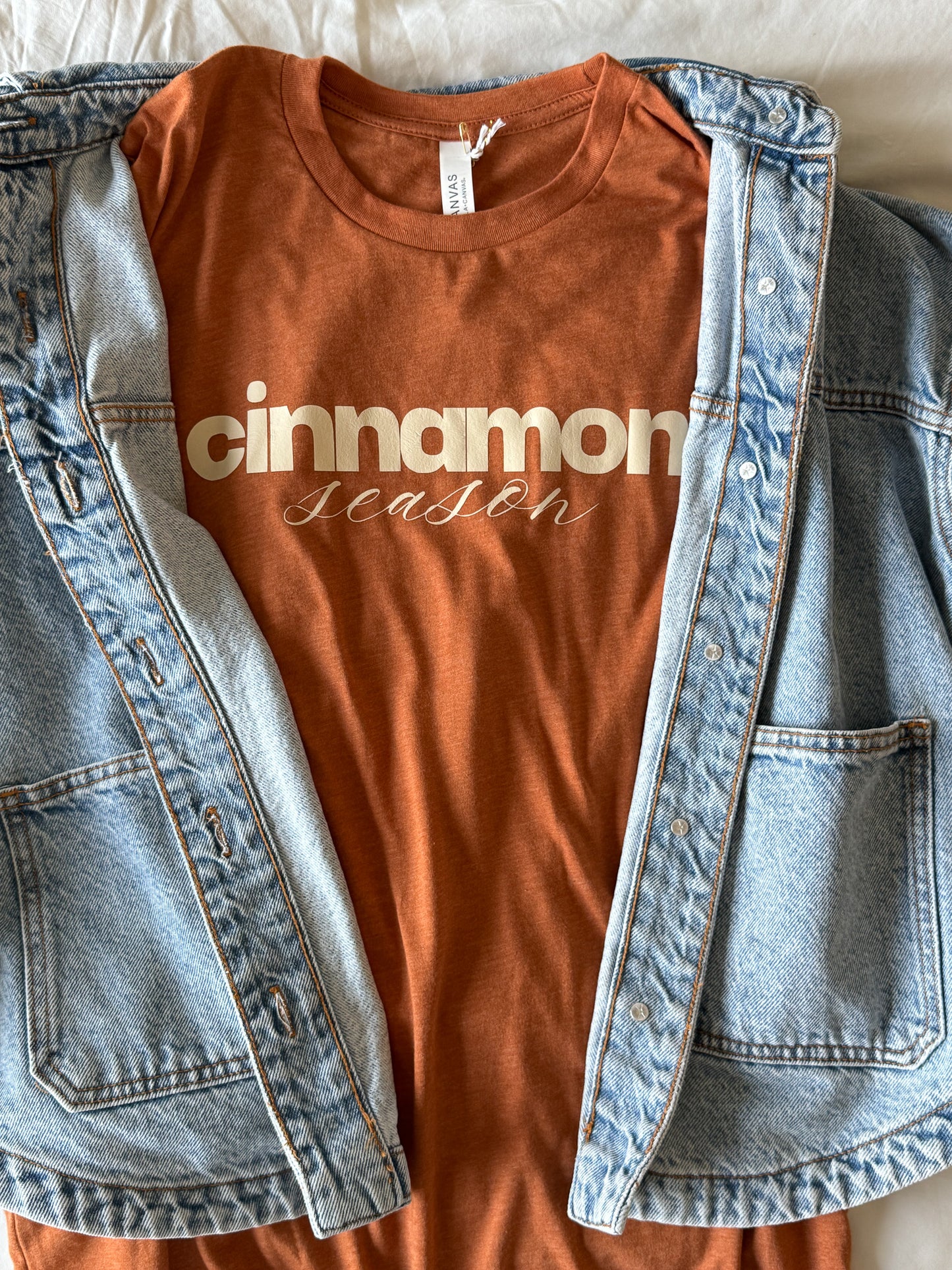Burnt orange t-shirt with 'cinnamon season' text inside a denim jacket