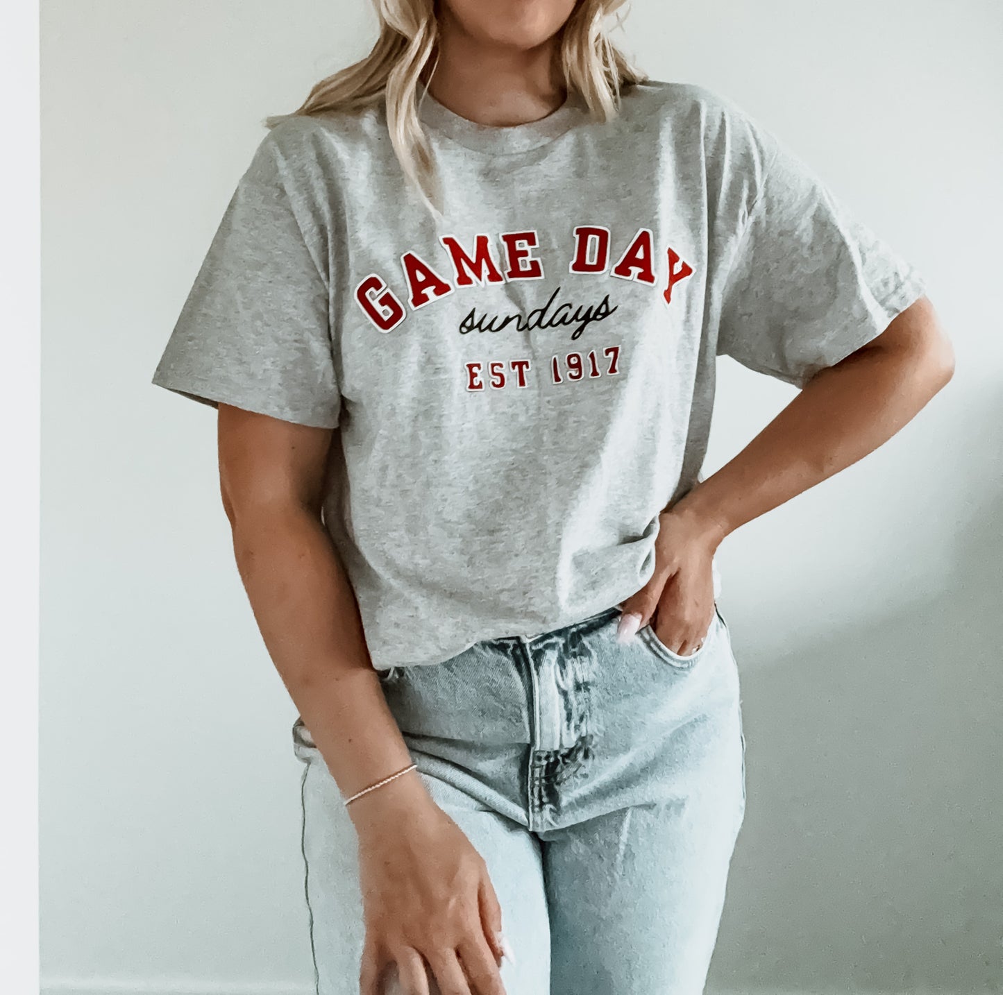 Person wearing a gray t-shirt with 'GAME DAY sundays EST 1917' text on a plain background