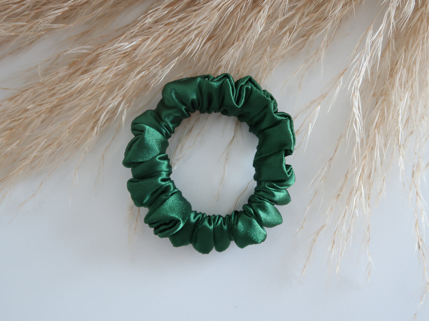 Green satin scrunchie on a light background with dried grasses