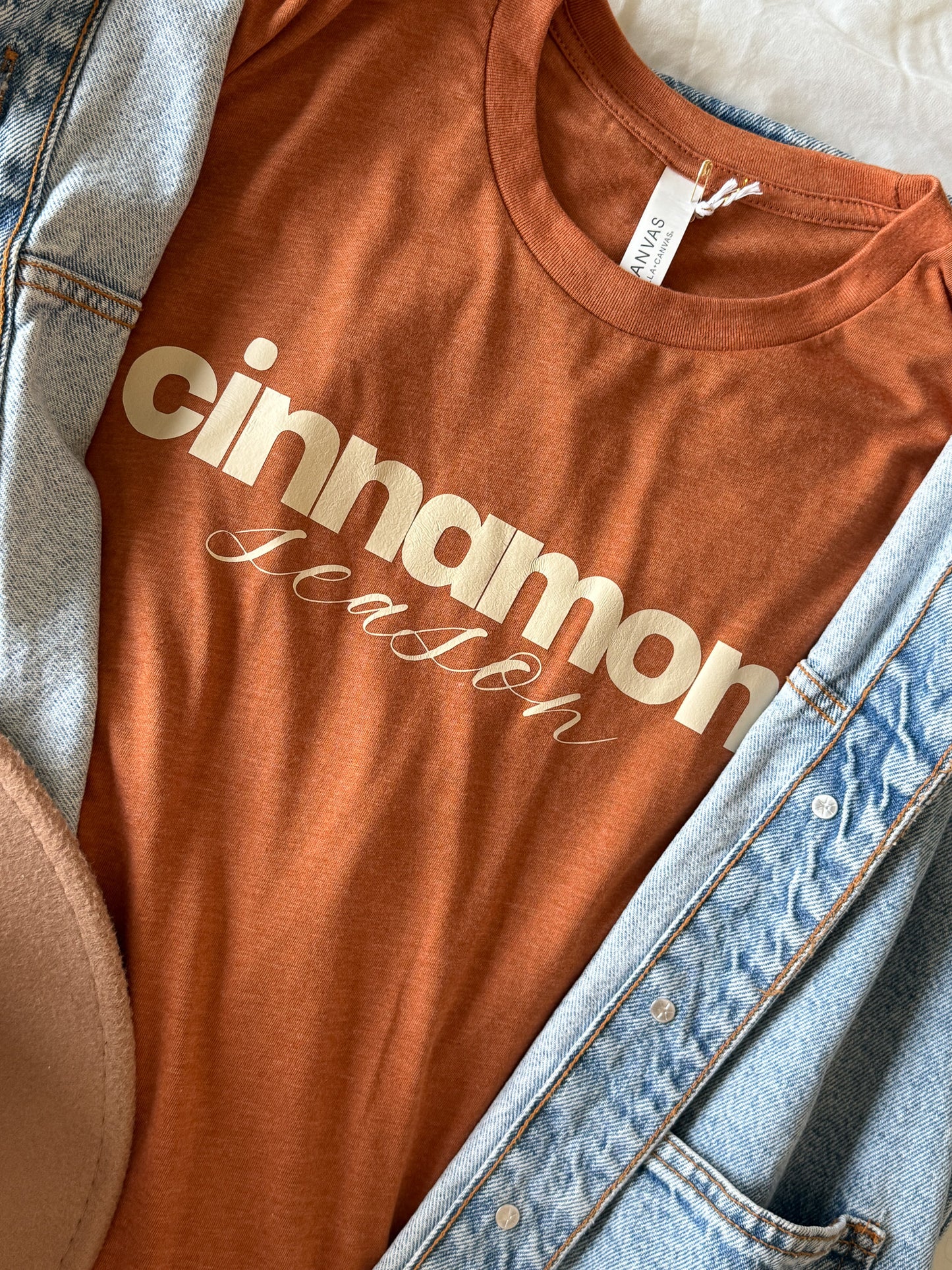 Burnt orange & beige t-shirt with 'cinnamon season' text on a denim jacket background
