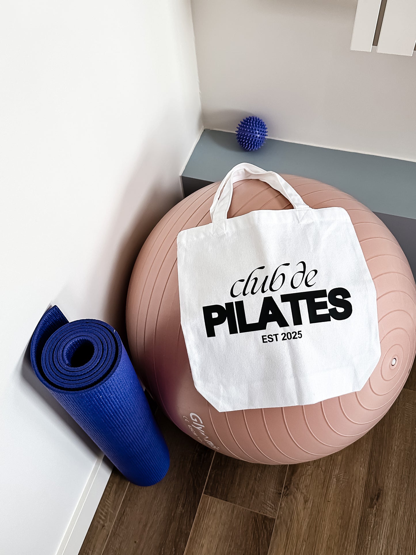 Tote bag with 'club de PILATES EST 2025' text on a Pilates ball and yoga mat.