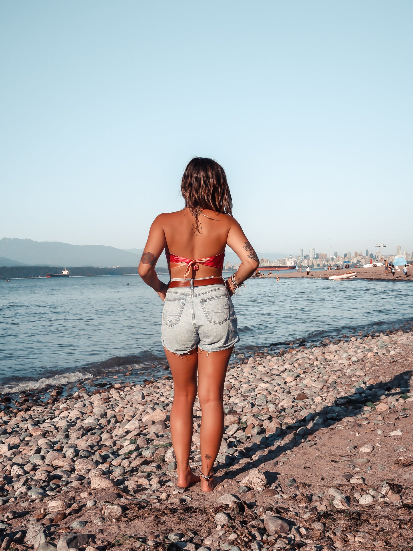 back of woman standing on beach wearing pink and orange bandeau top and jean shorts