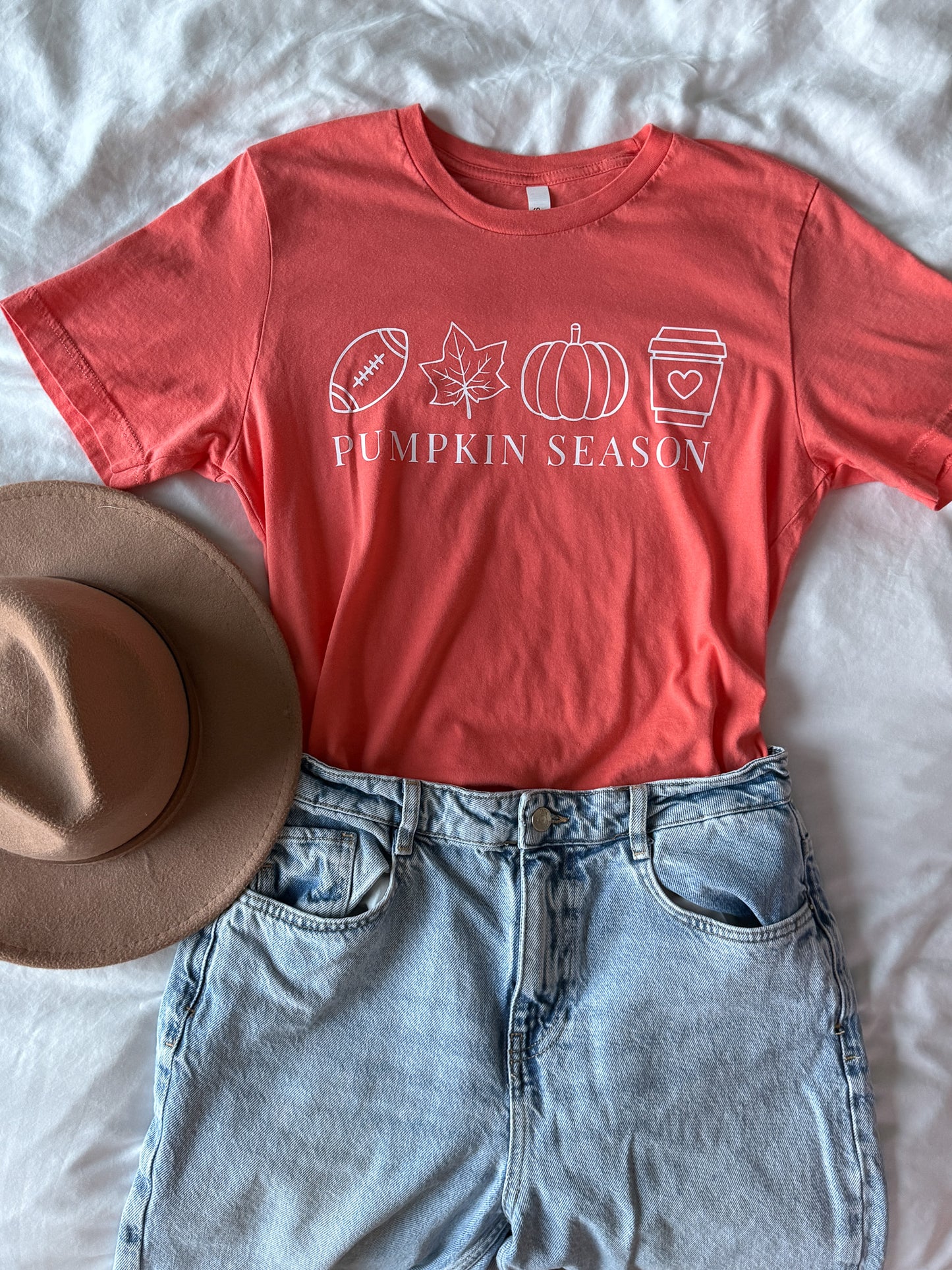 coral orange t-shirt with 'Pumpkin Season' design, denim shorts, and a hat on a light background
