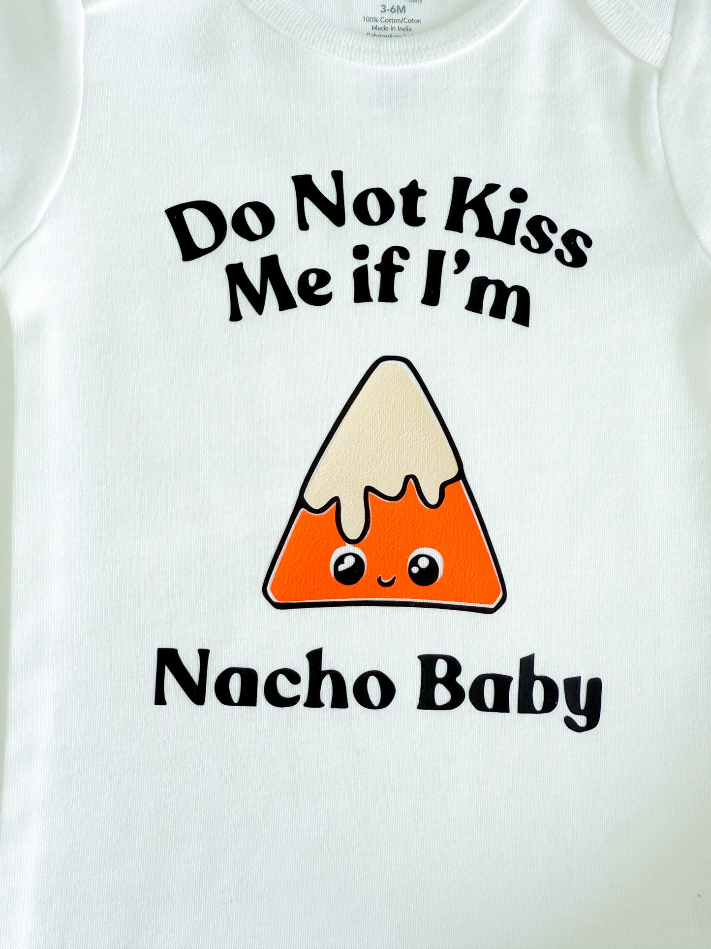 White baby onesie with nacho graphic and text 'Do Not Kiss Me if I'm Nacho Baby' on a white background