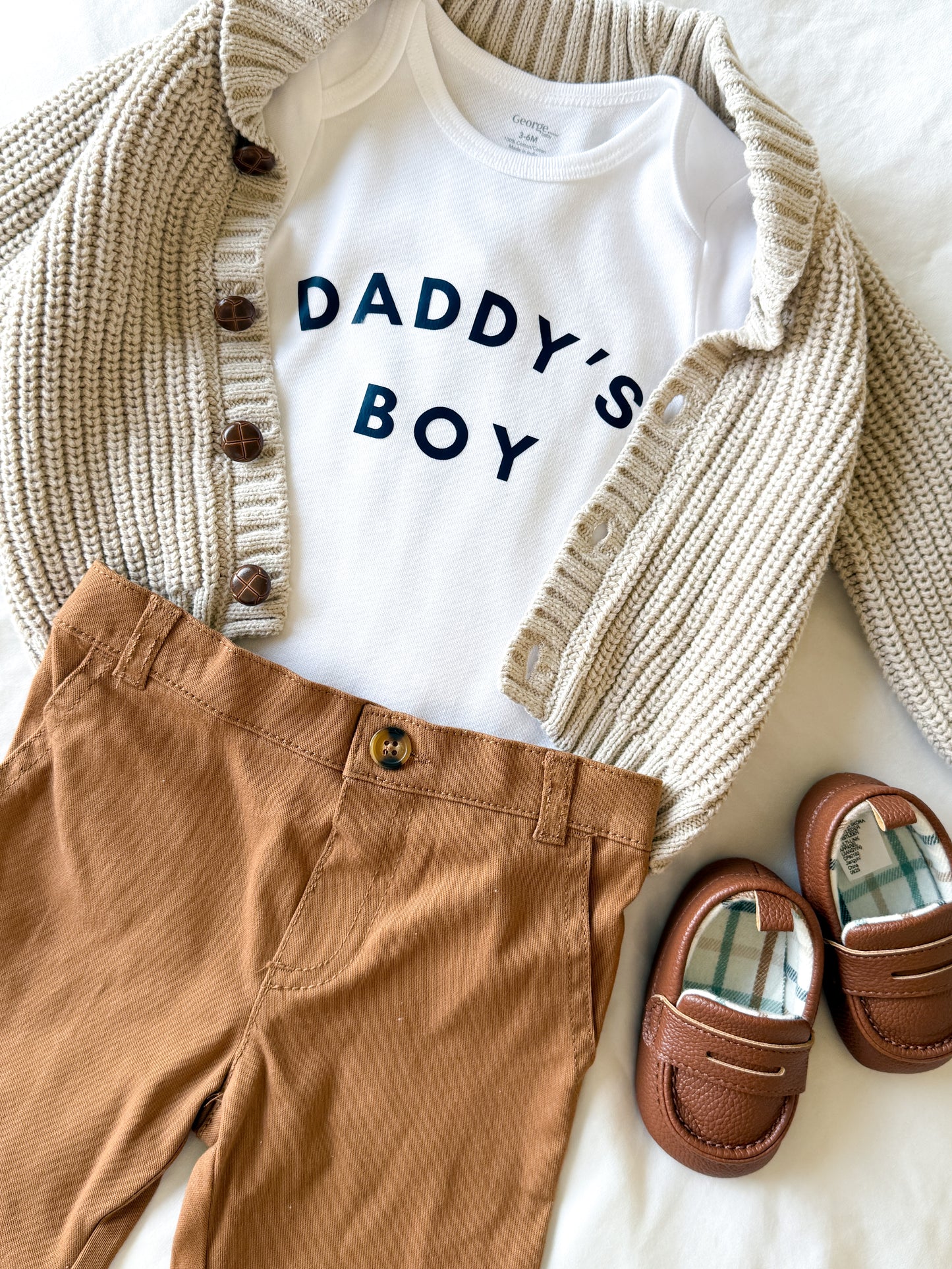 Children's outfit with 'Daddy's Boy' shirt, brown pants, and shoes on a white background