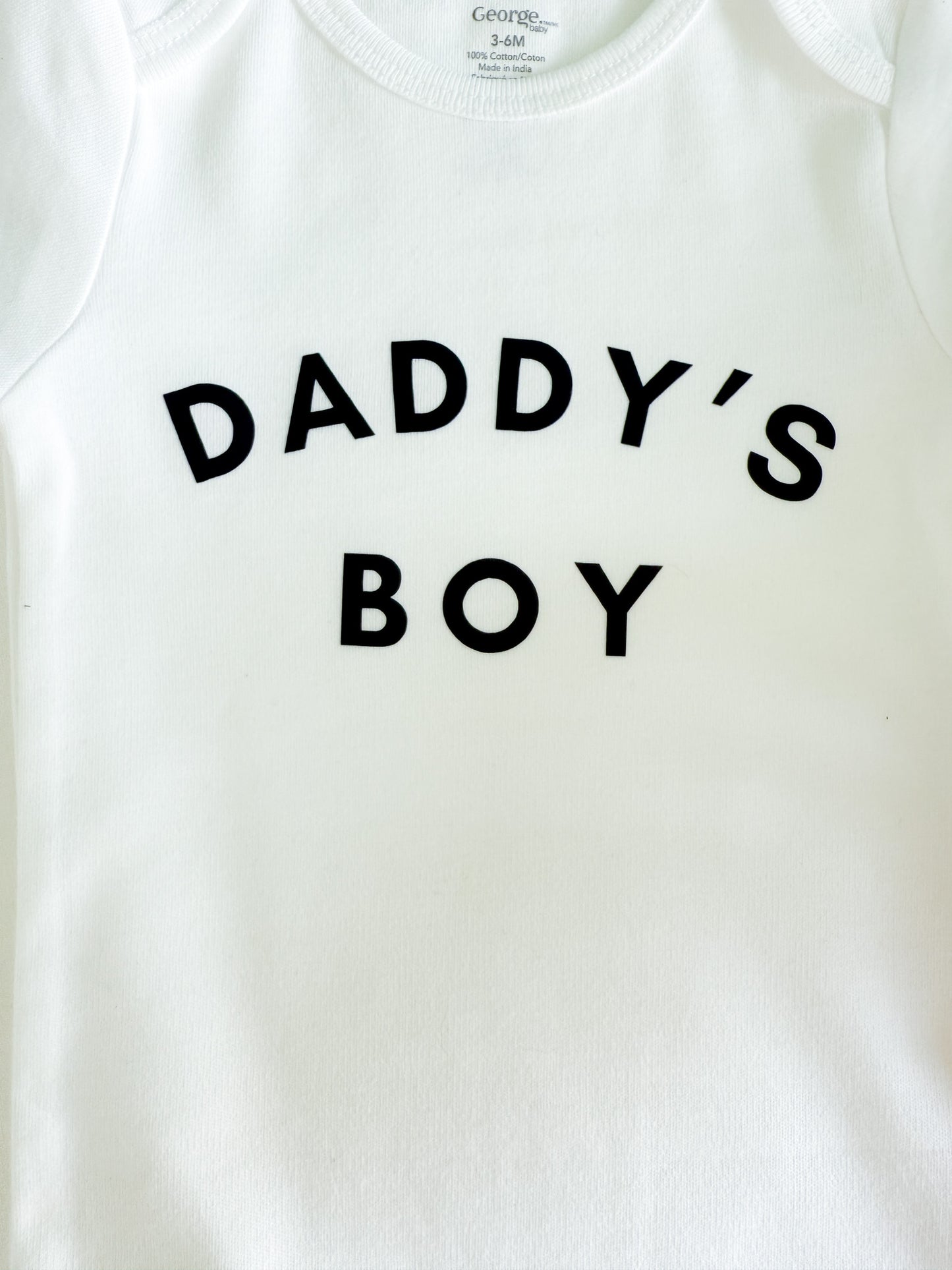 White baby onesie with 'DADDY'S BOY' text on a plain background