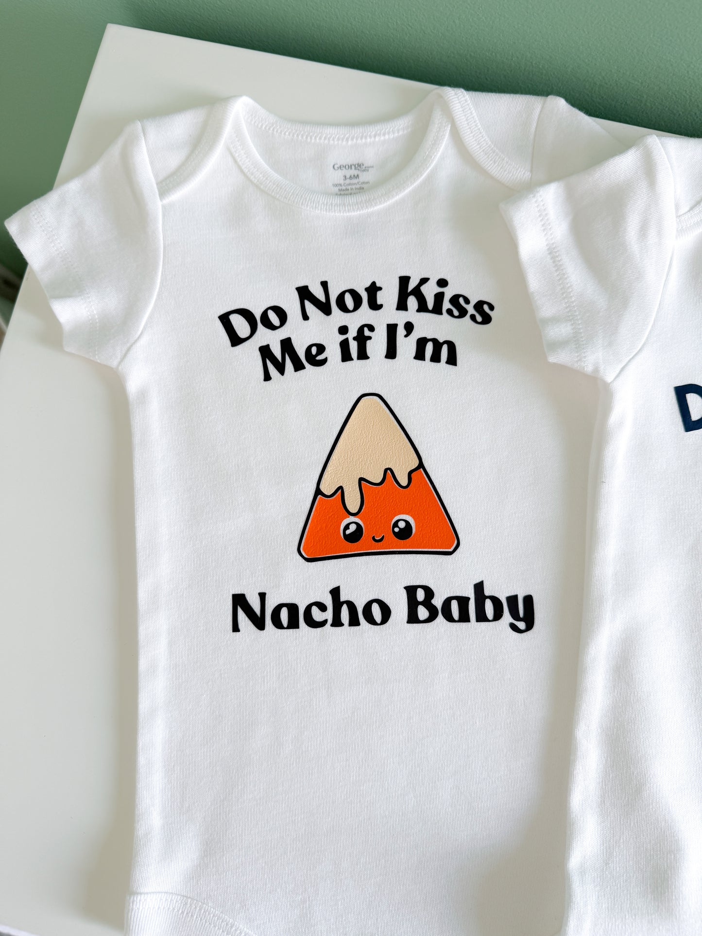 White baby onesie with nacho design and text on a white background