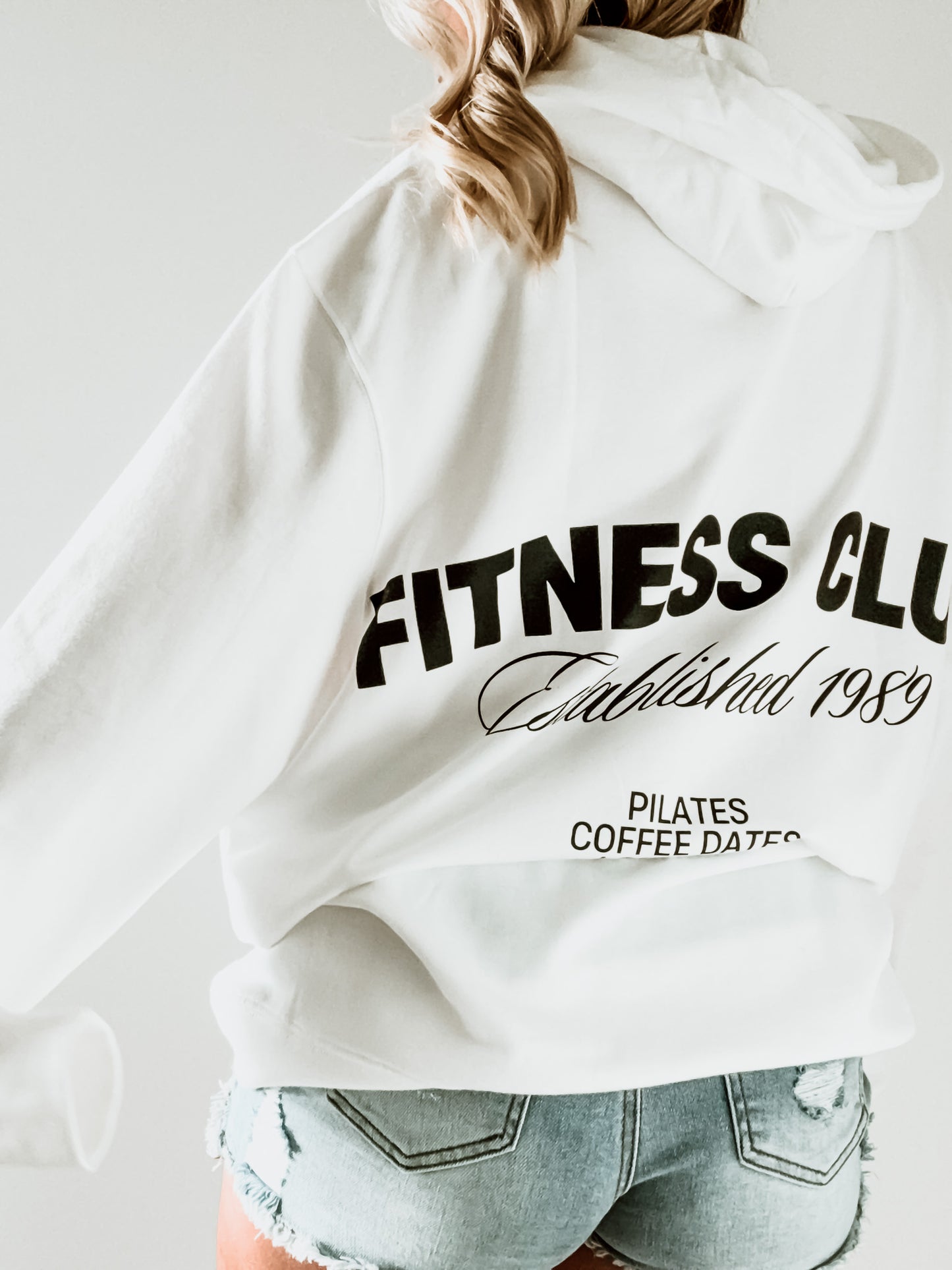 White hoodie with 'Fitness Club' text on the back, worn by a person.