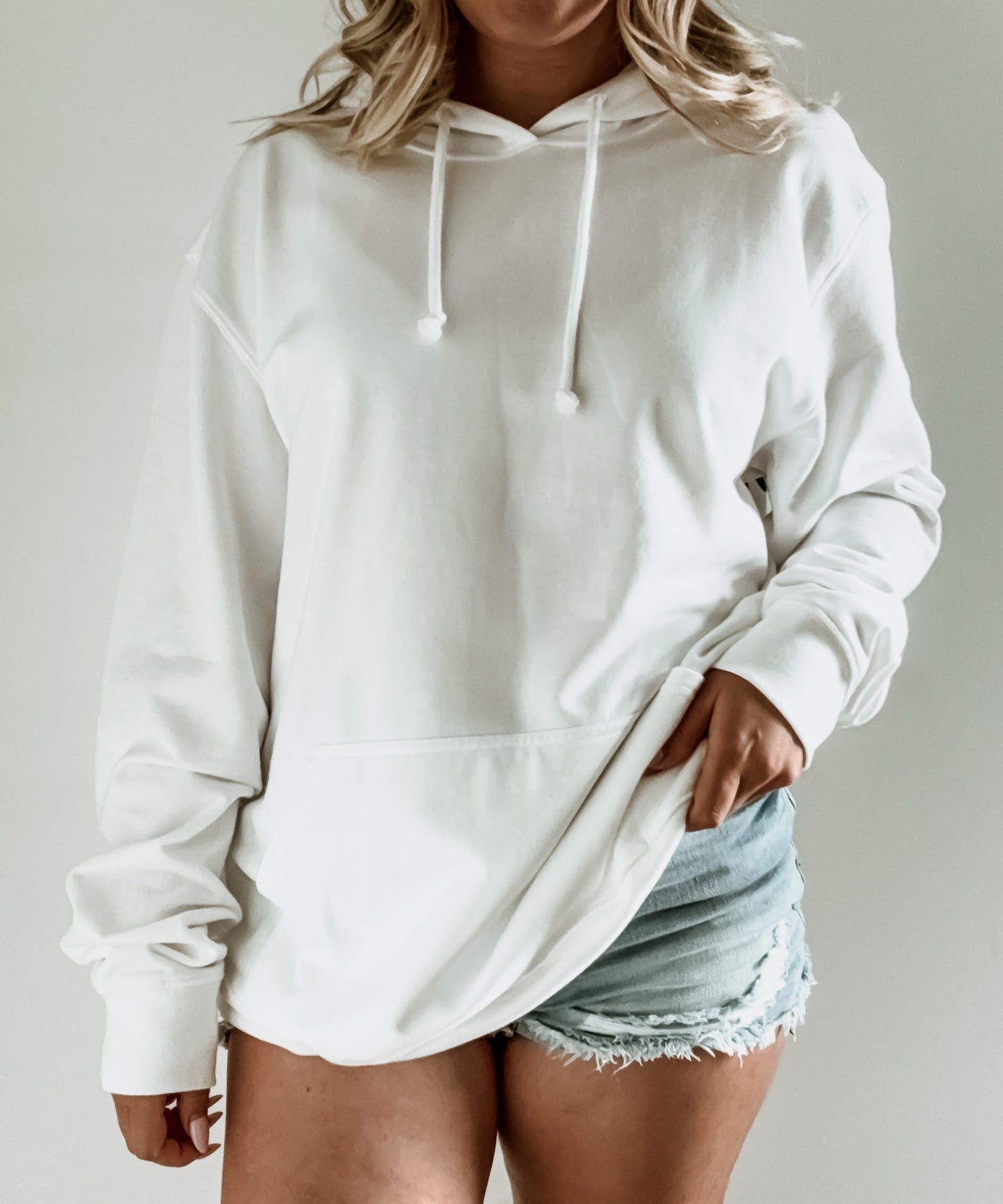 Person wearing a white hoodie and denim shorts on a plain background