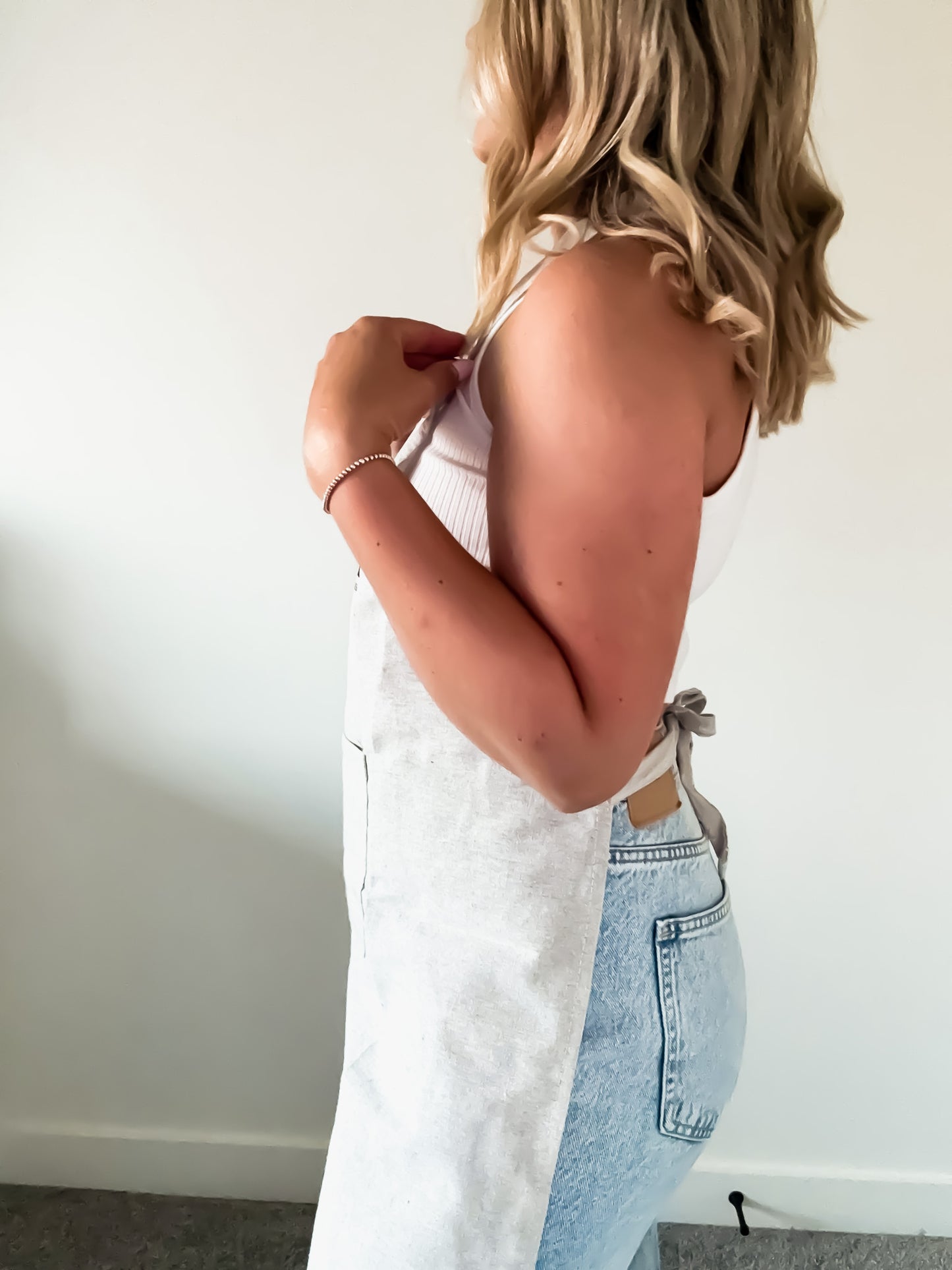 Person wearing a light grey apron over a light blue denim dress against a plain background