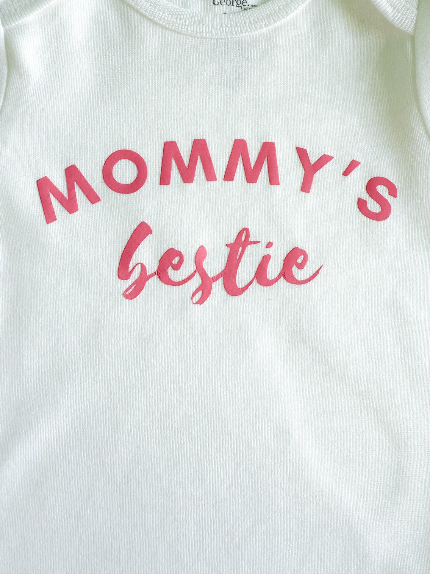 White baby onesie with pink text 'Mommy's bestie' on a white background