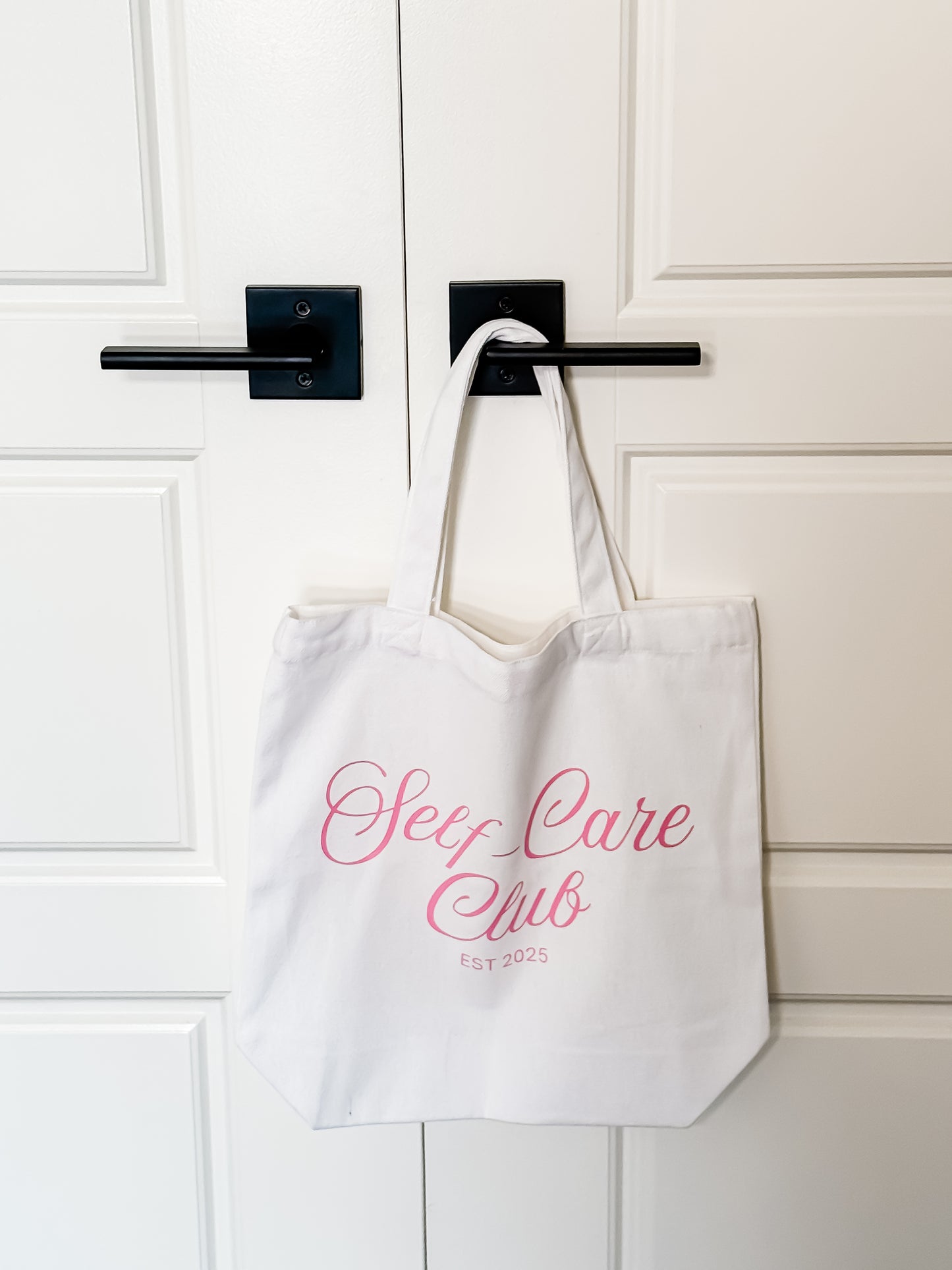 White tote bag with 'Sex Care Club' text hanging on a door handle.