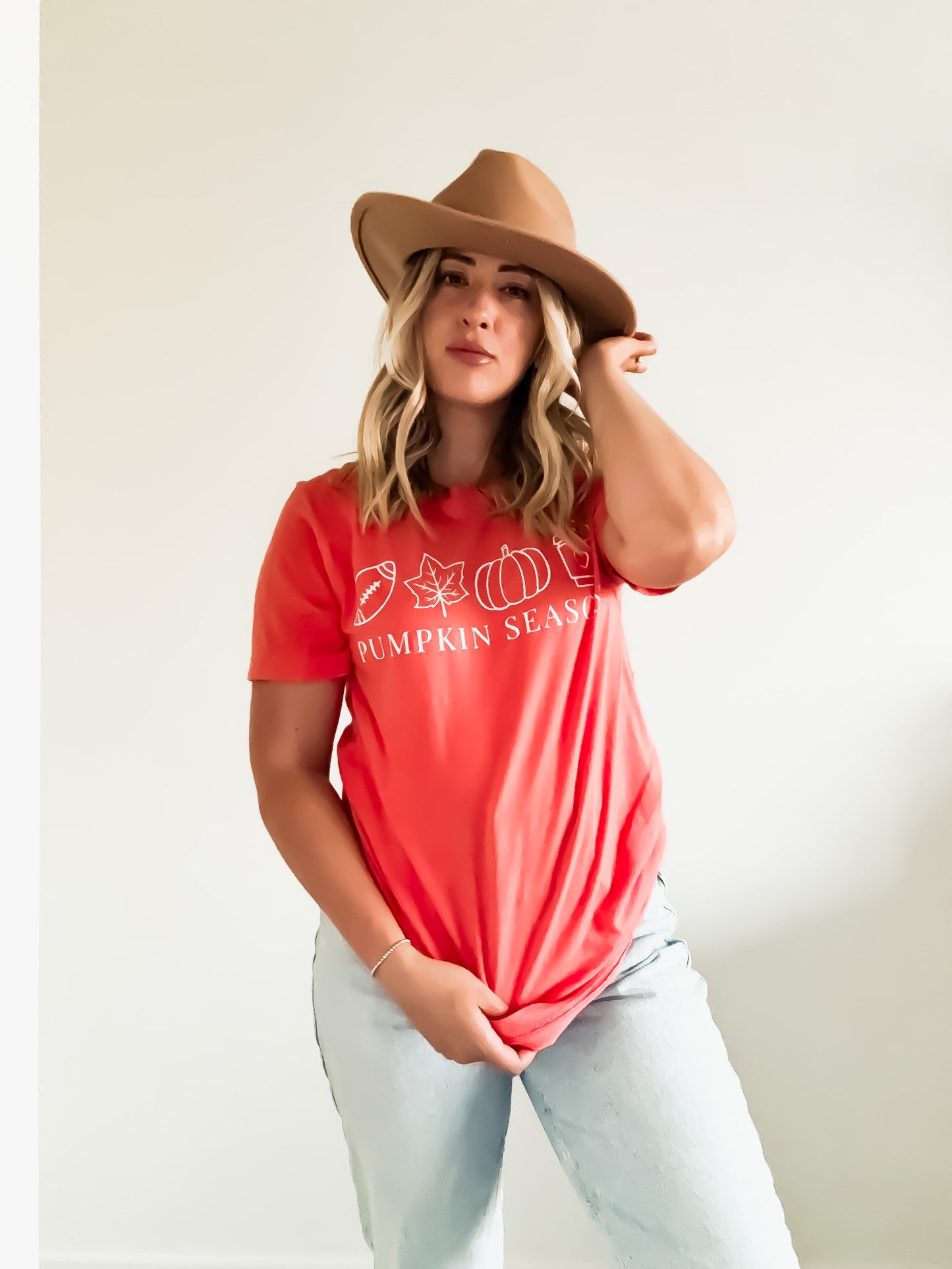 Woman wearing a red 'Pumpkin Season' t-shirt and brown hat against a plain background