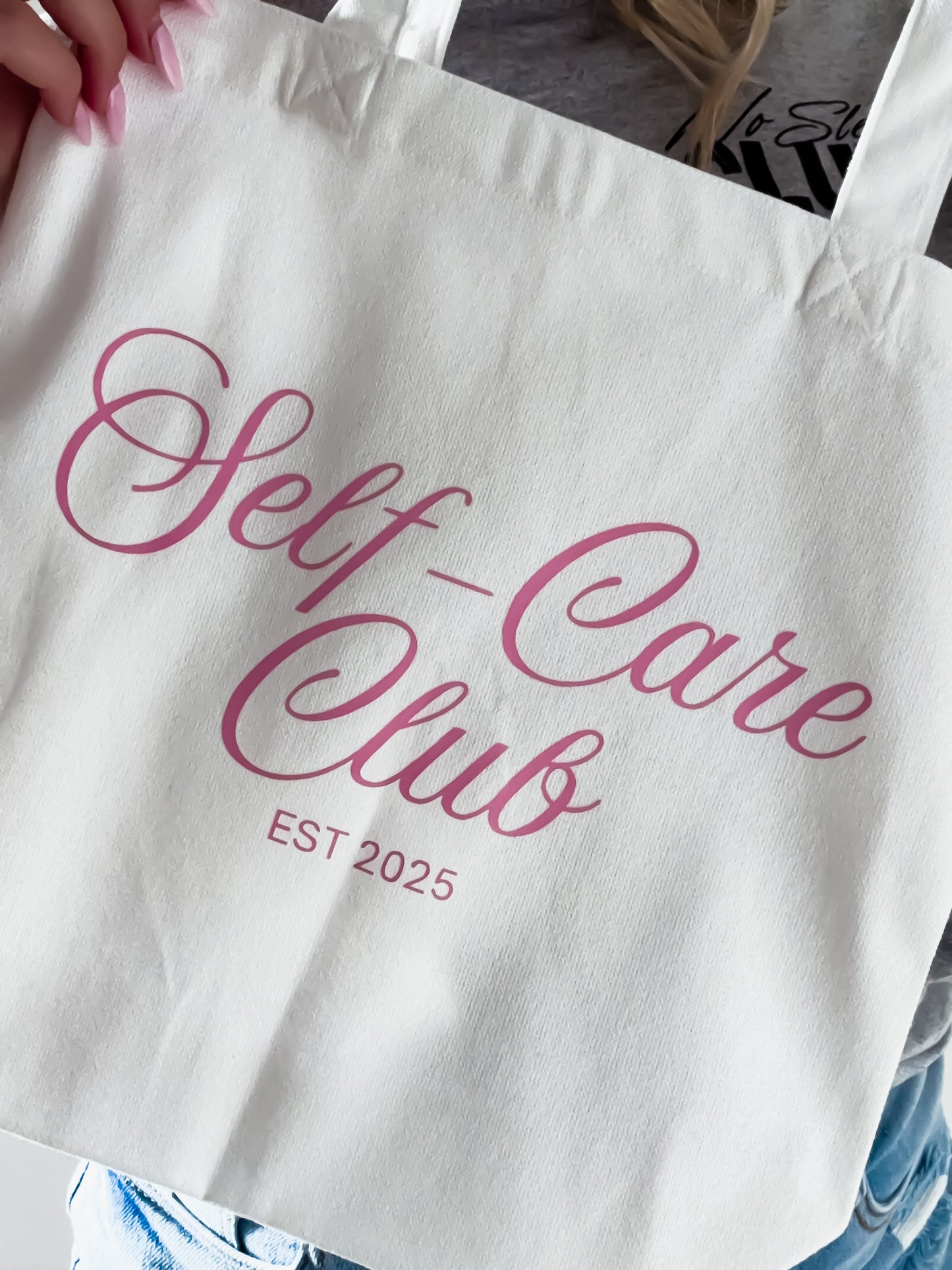Tote bag with 'Self-Care Club EST 2025' text in pink on a white background