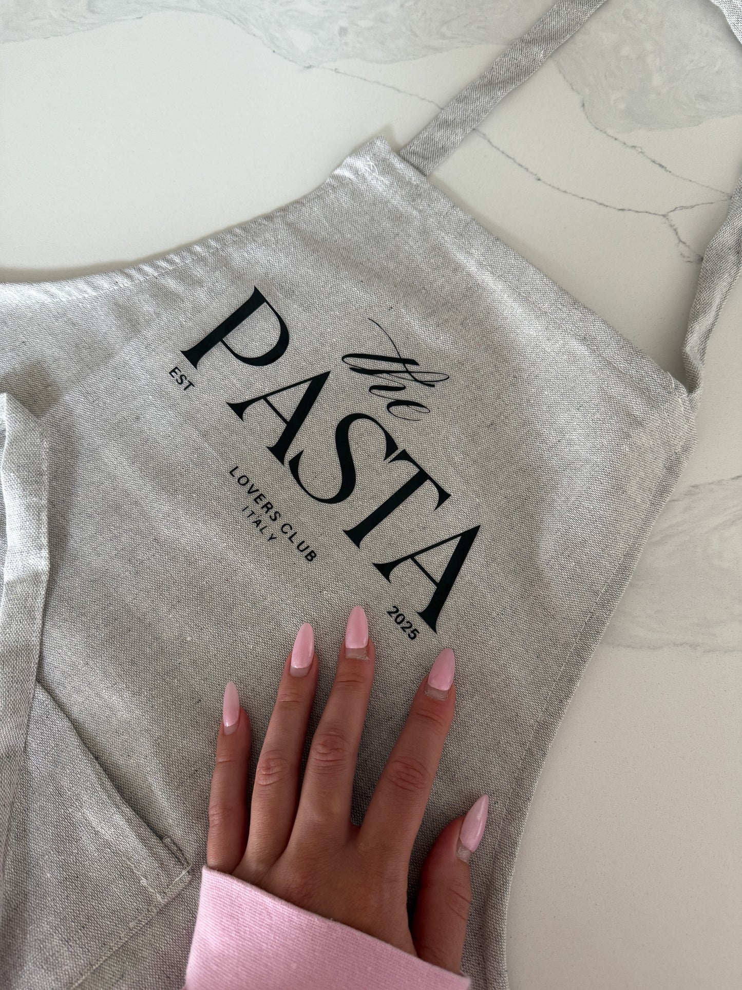 Gray apron with 'The Pasta Lovers Club' text on a marble surface.