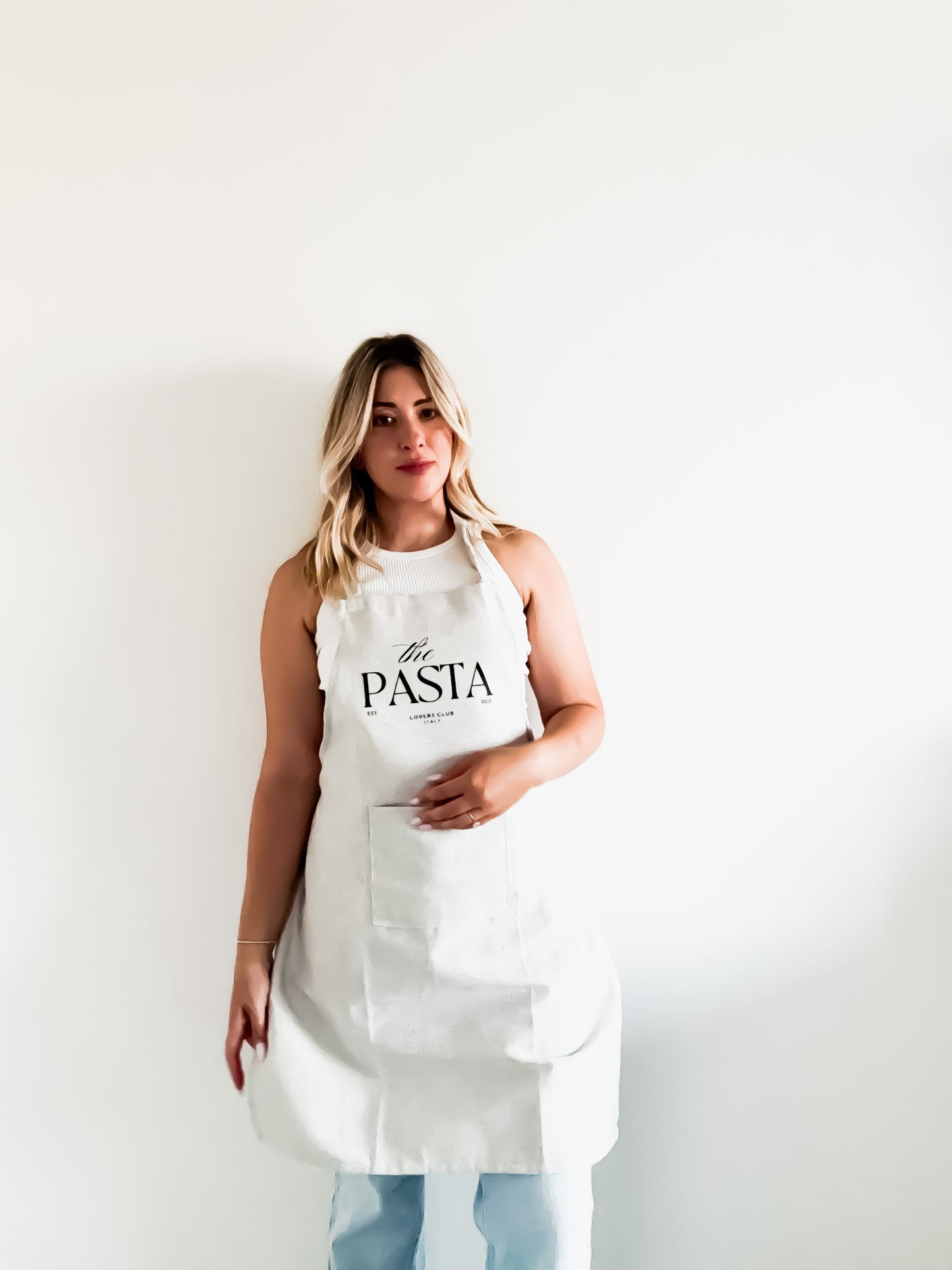 Woman wearing a white apron with 'the PASTA lovers club' text on a plain background