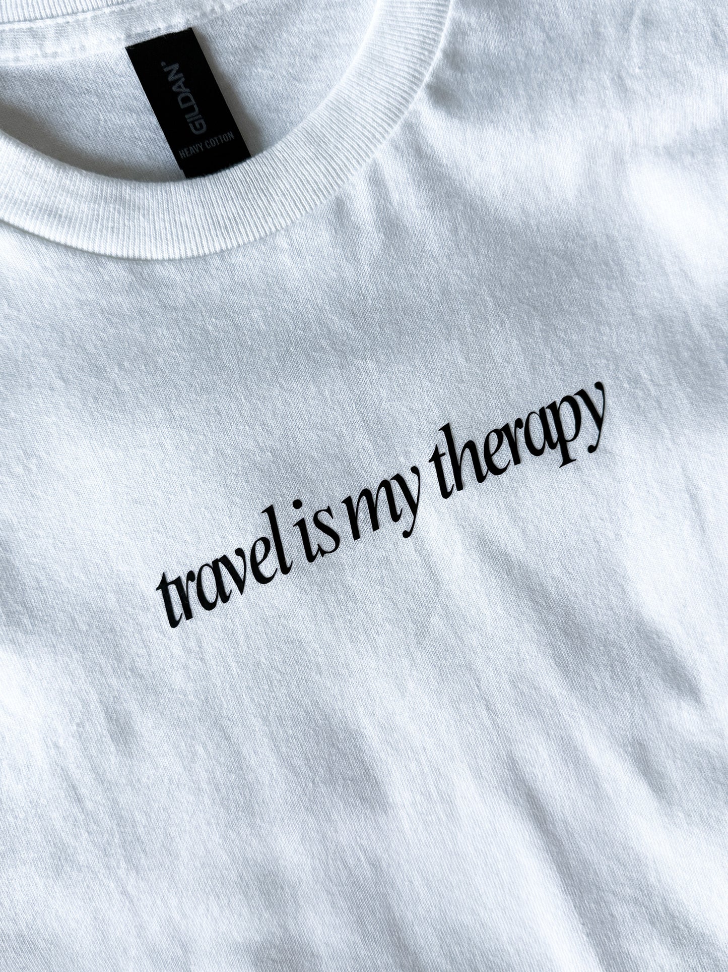 White sweatshirt with 'travel is my therapy' text on a plain background