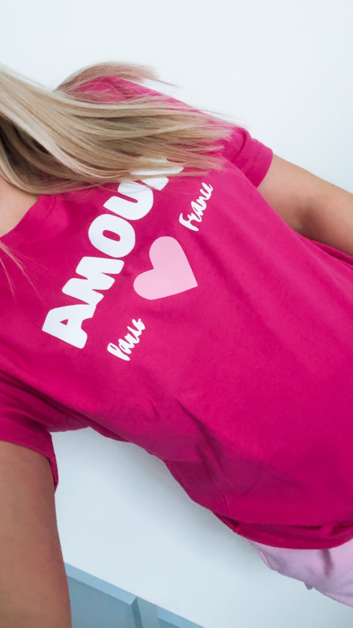 Person wearing a bright pink t-shirt with text and a heart design.