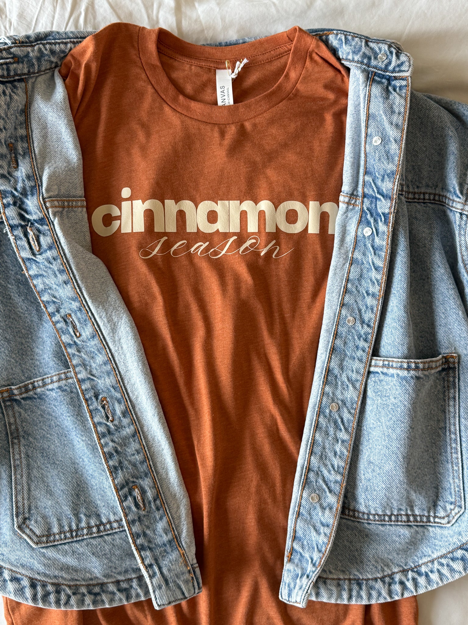 Burnt orange t-shirt with 'cinnamon season' text inside a denim jacket