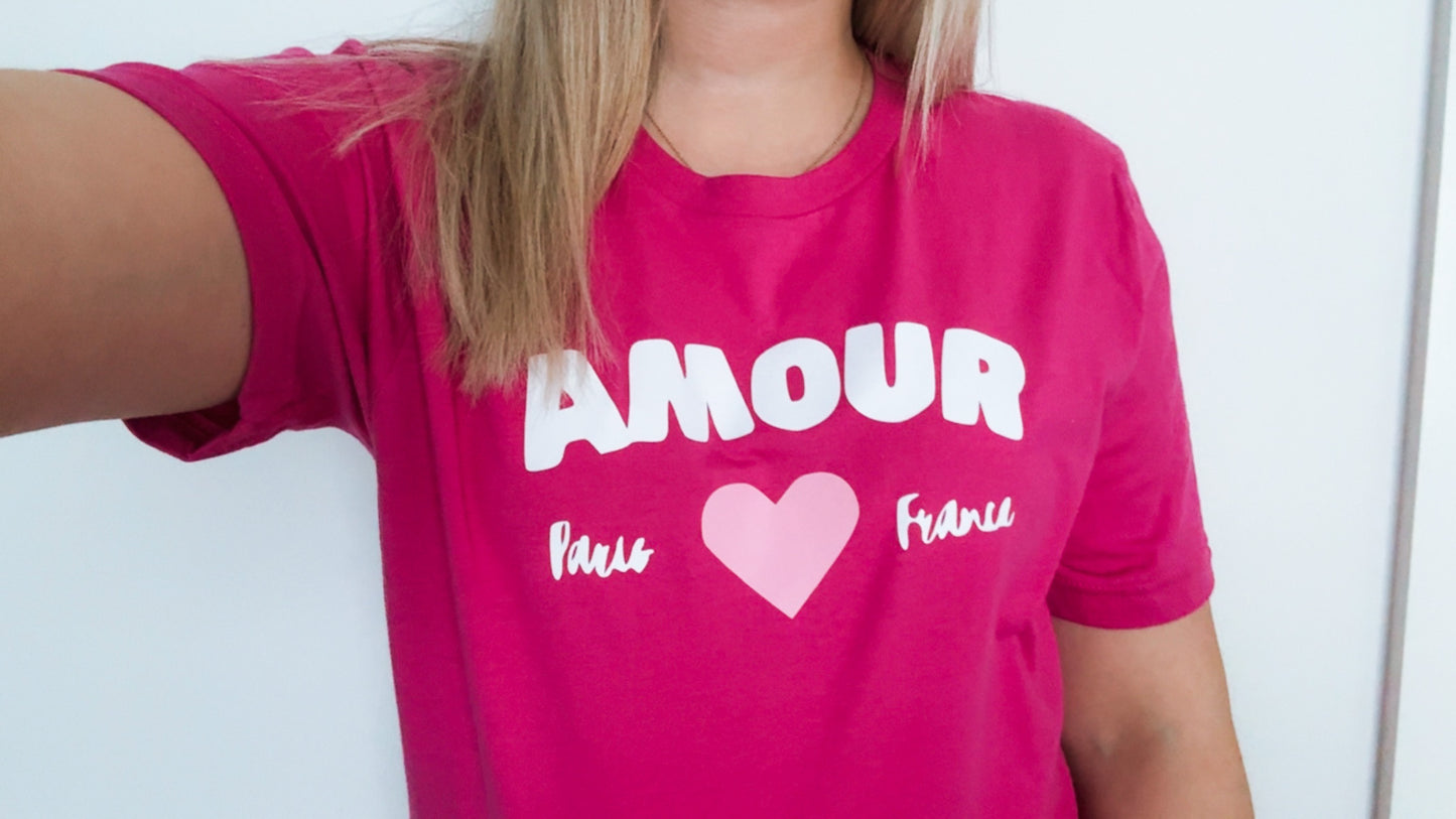 Person wearing a pink t-shirt with 'AMOUR' and heart design on a plain background