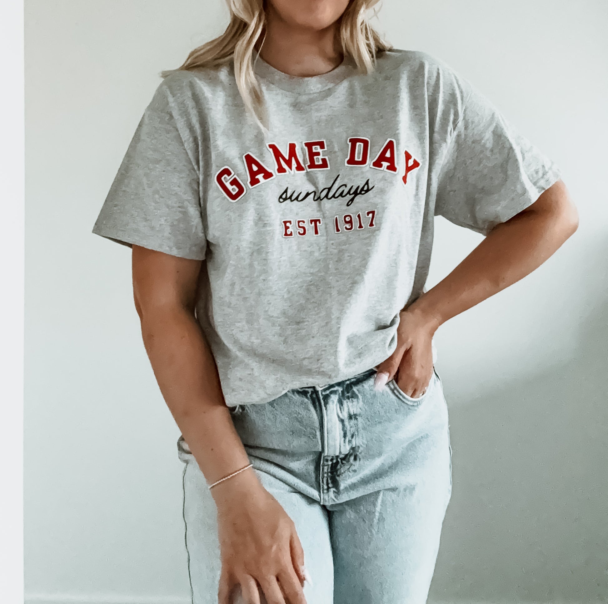 Person wearing a gray t-shirt with 'GAME DAY sundays EST 1917' text on a plain background