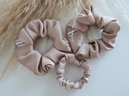 Three pink scrunchies on a light background with a fluffy beige texture.