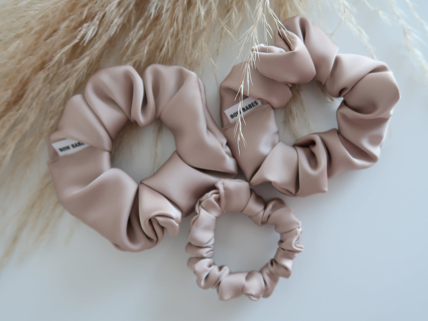 Three Champagne  pink scrunchies on a light background with a fluffy beige texture.
