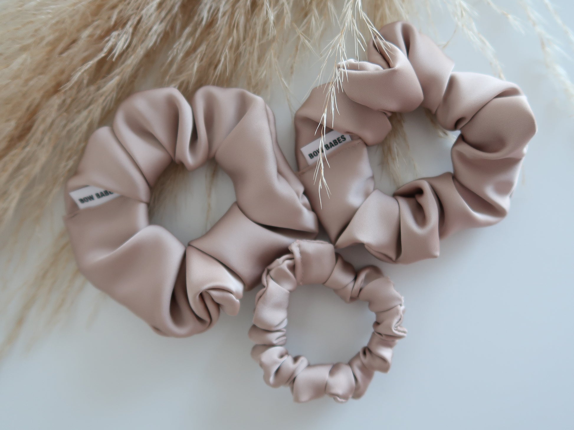Three Champagne  pink scrunchies on a light background with a fluffy beige texture.