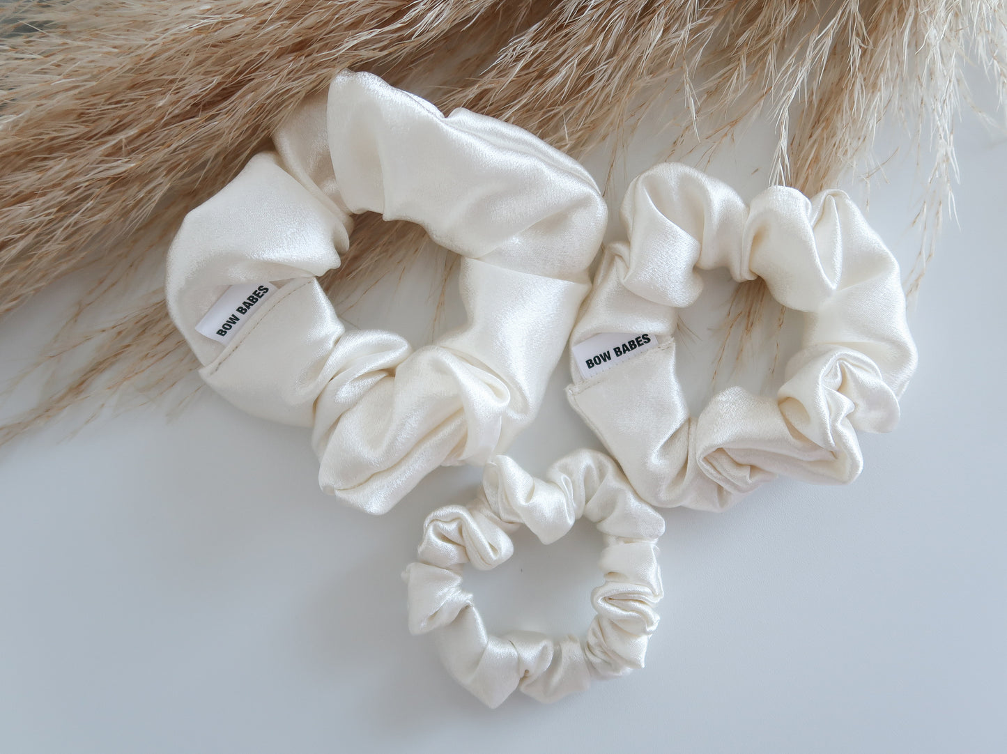 Set of cream-colored scrunchies with brand label on a light background