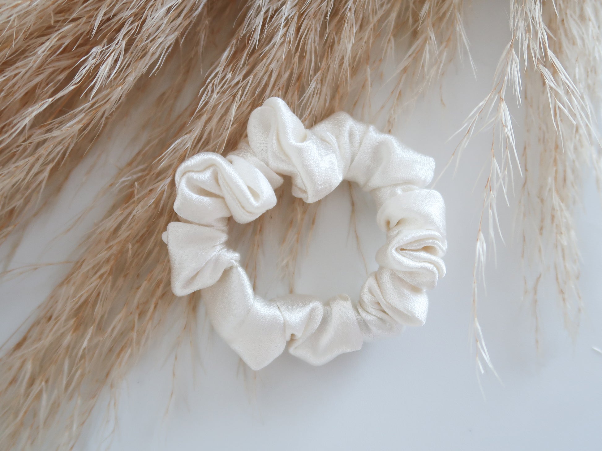 white scrunchie on a light background with dried grasses.