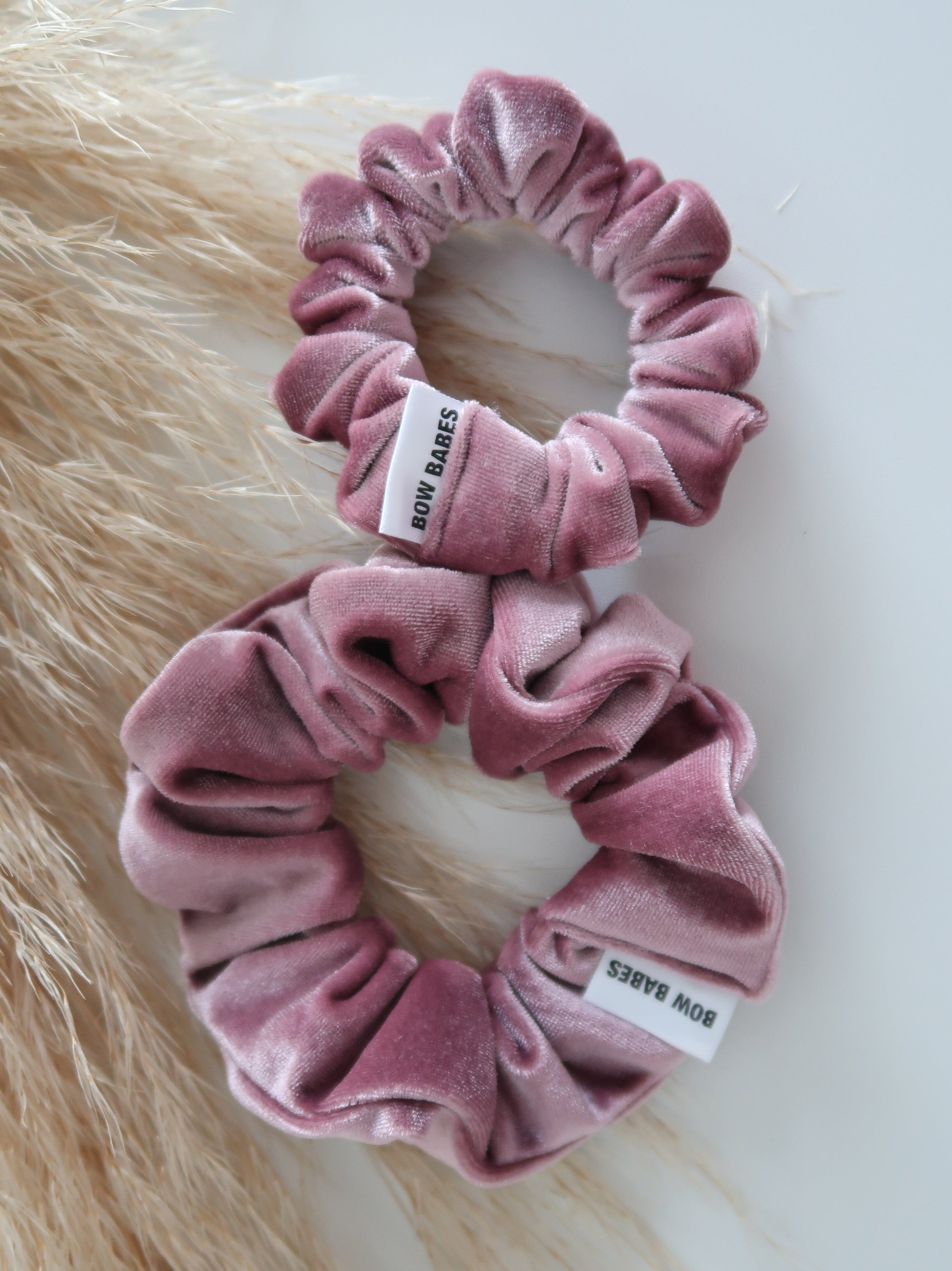 Pink velvet scrunchies with brand label on a fur surface