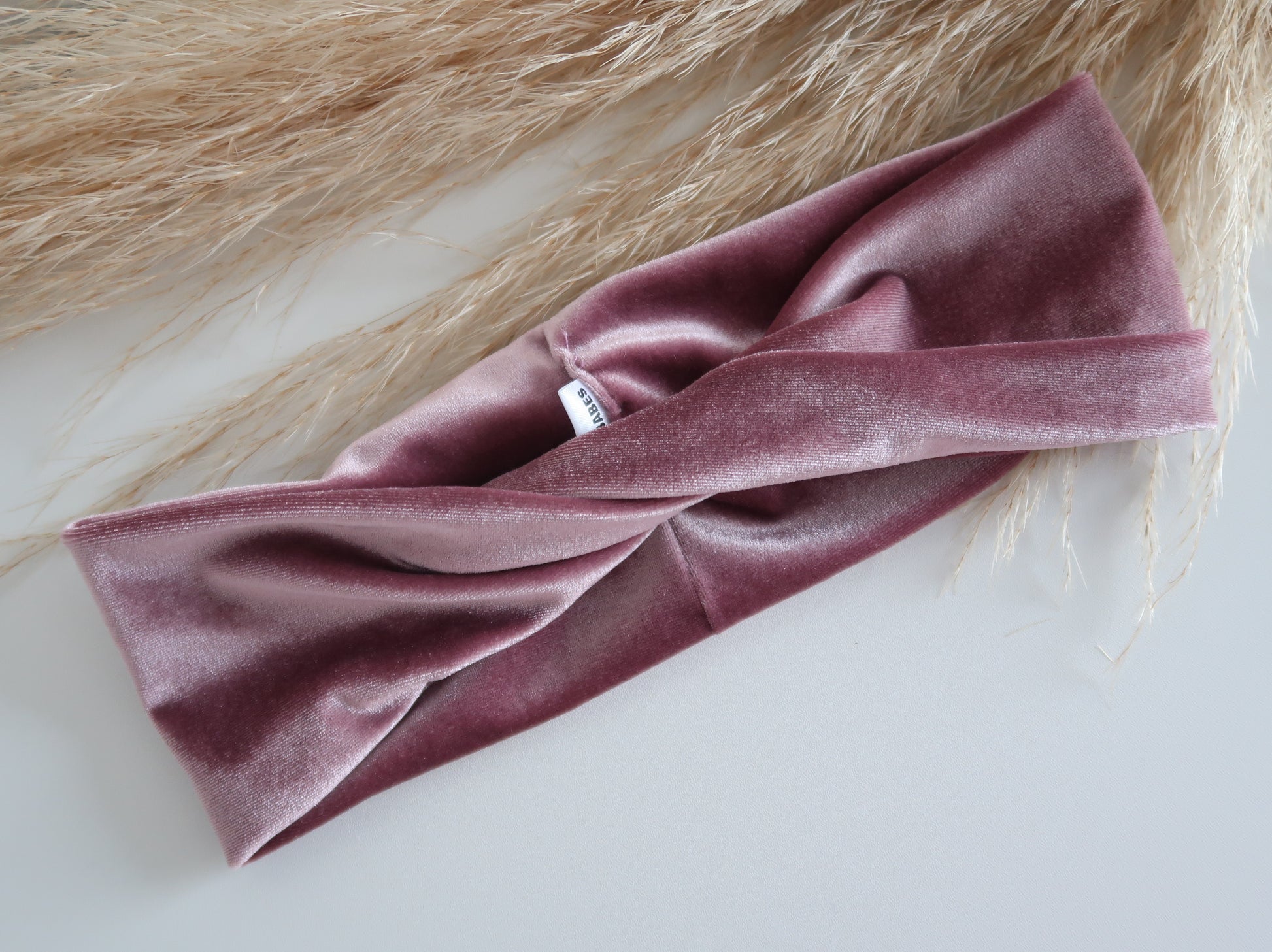Pink velvet headband on a white surface with a textured beige background