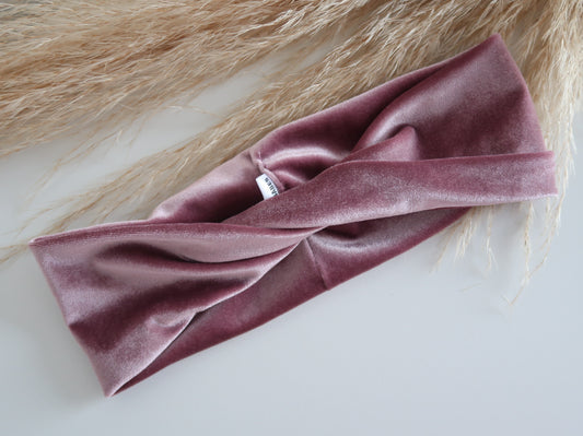 Pink velvet headband on a white surface with a textured beige background