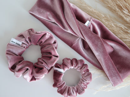 Pink velvet hair accessories including a headband and two scrunchies on a light background.