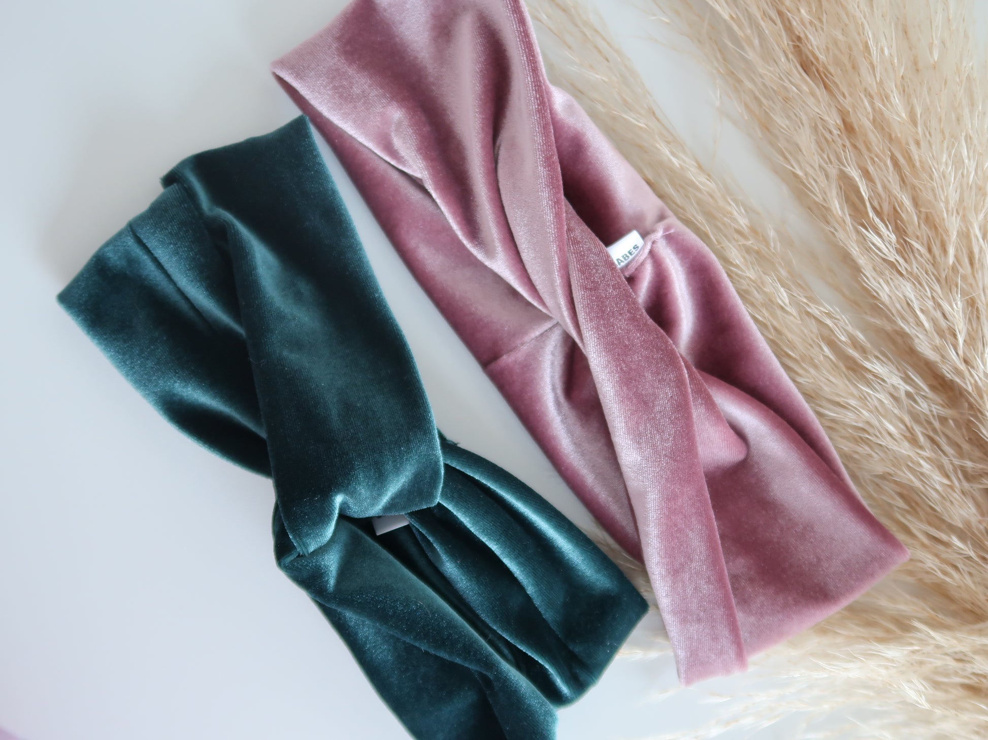 Two velvet headbands, one green and one pink, on a textured surface.