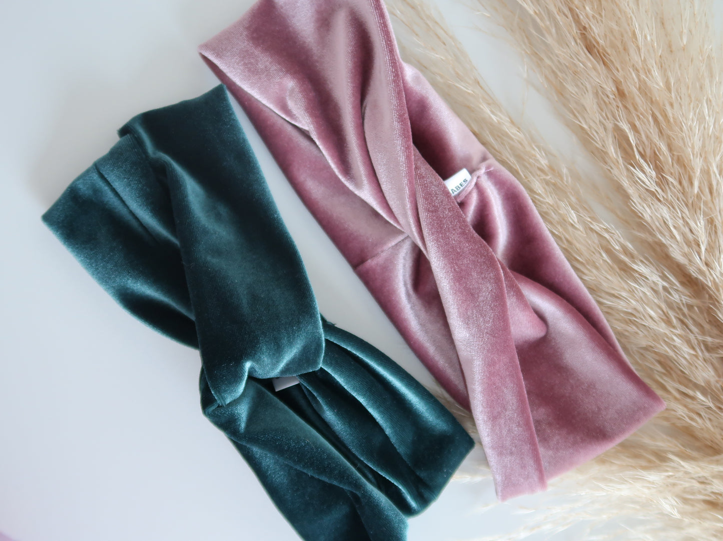 Two velvet headbands, one green and one pink, on a textured surface.
