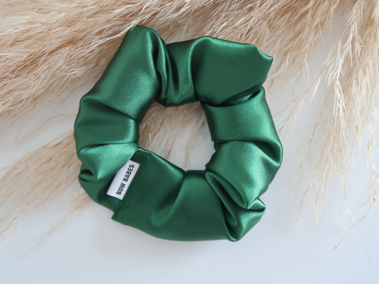 Green satin scrunchie with a brand label on a light background