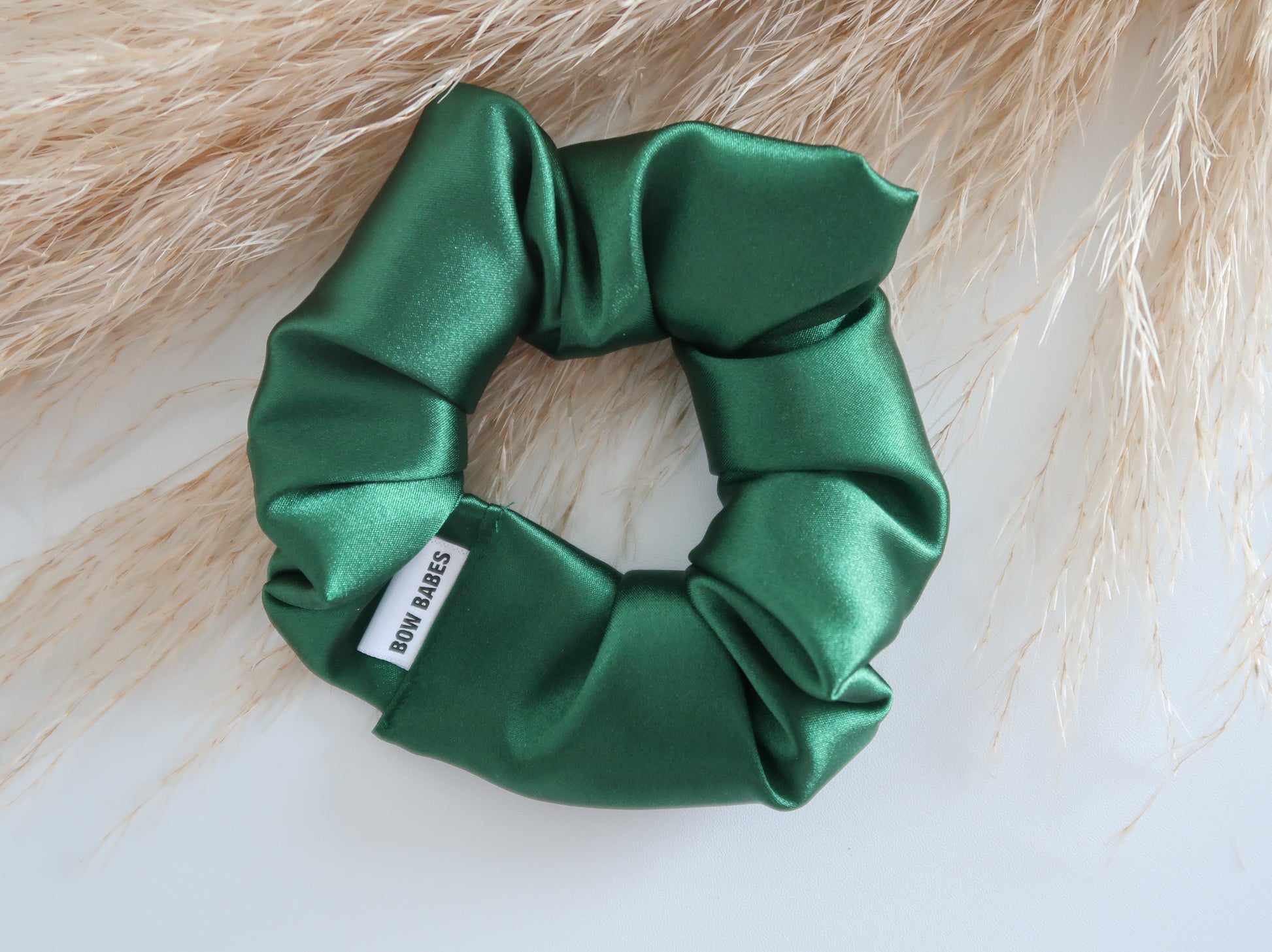 Green satin scrunchie with a brand label on a light background