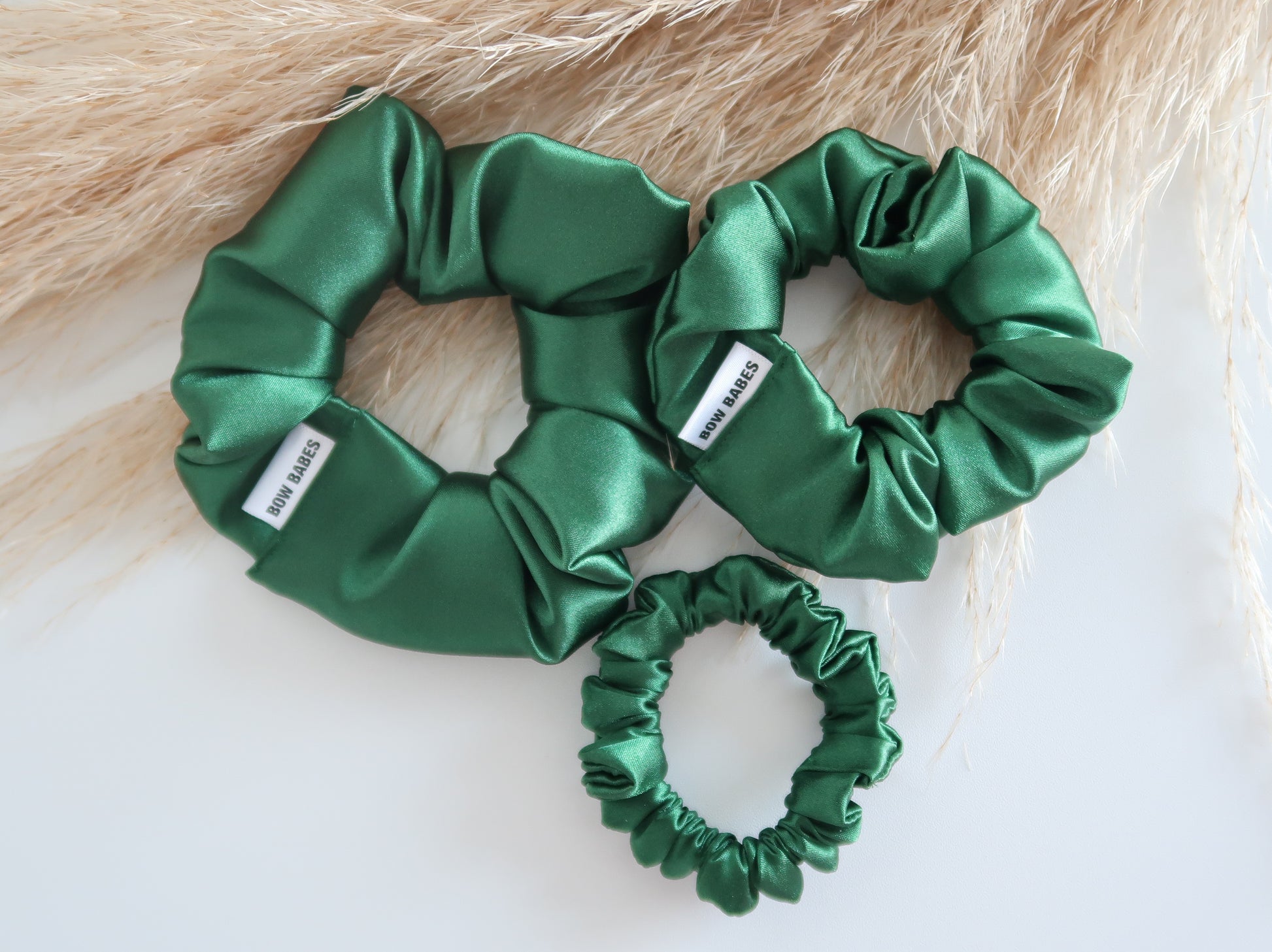 Three green satin scrunchies on a light wooden surface