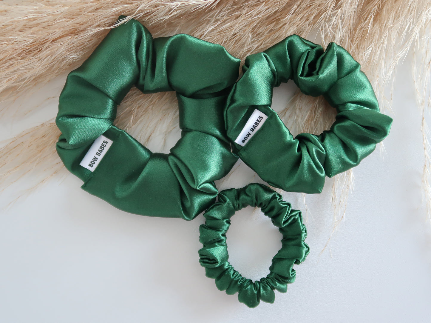 Three green satin scrunchies on a light wooden surface