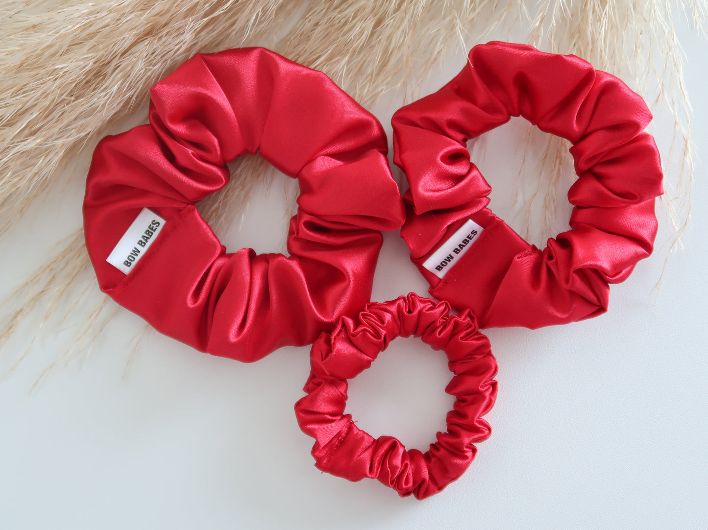 Three red satin scrunchies on a light wooden surface