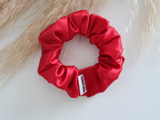 Red satin scrunchie with a brand label on a light background
