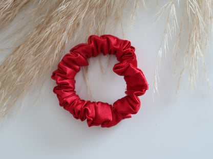Red satin scrunchie on a light background with dried grasses