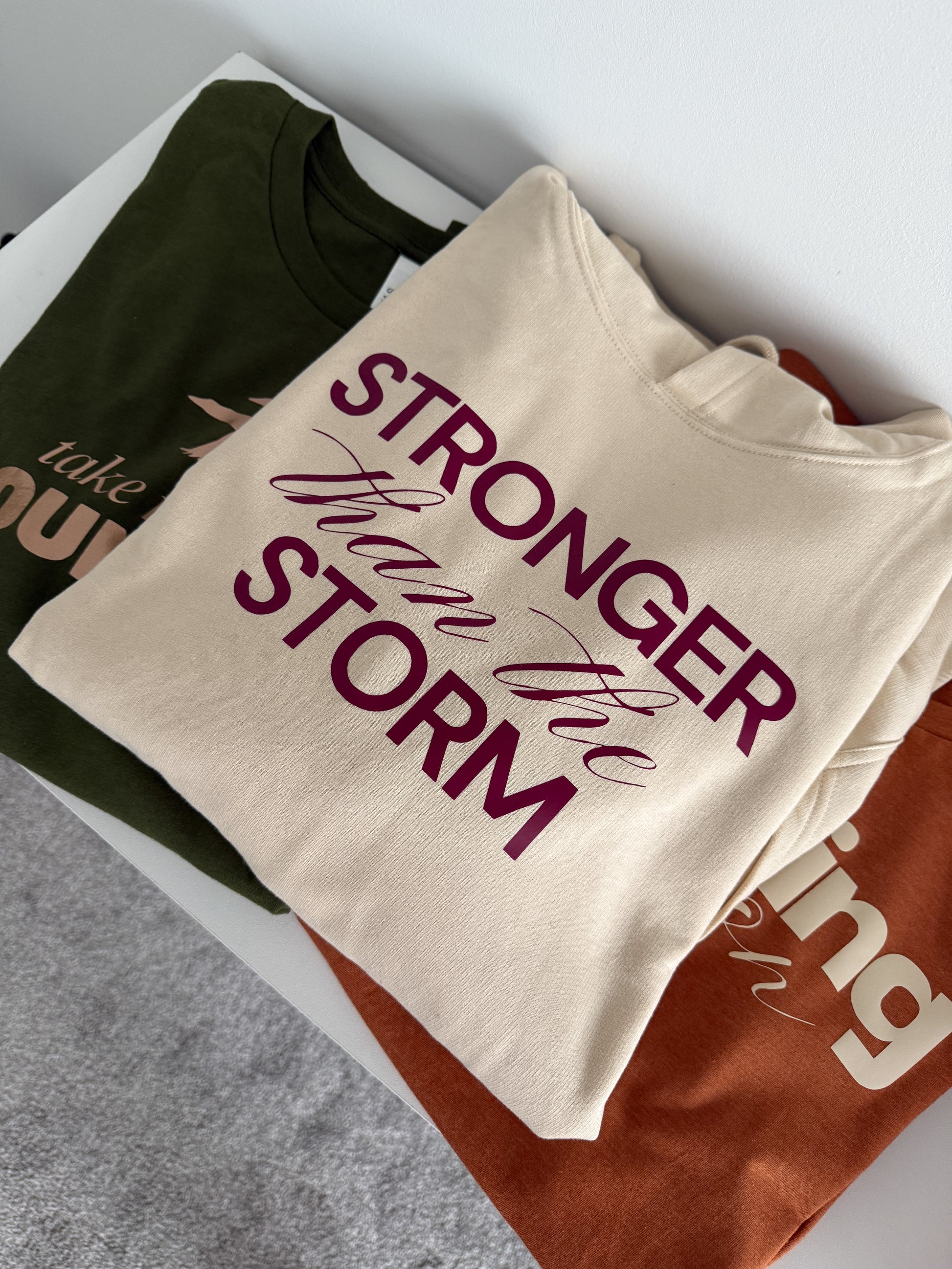 Folded t-shirt with 'Stronger than the storm' text on a gray surface