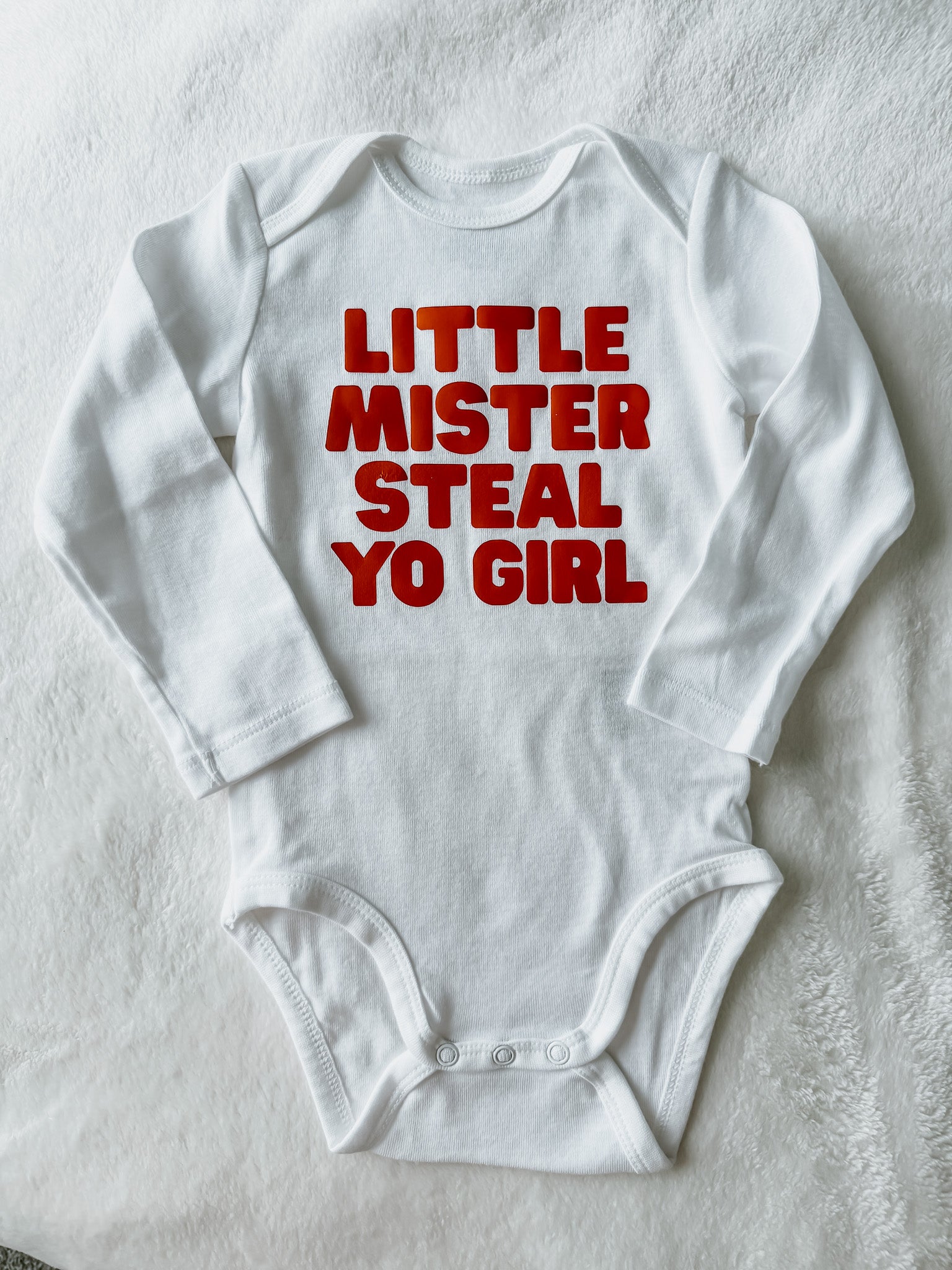 White baby onesie with red text on a light gray background