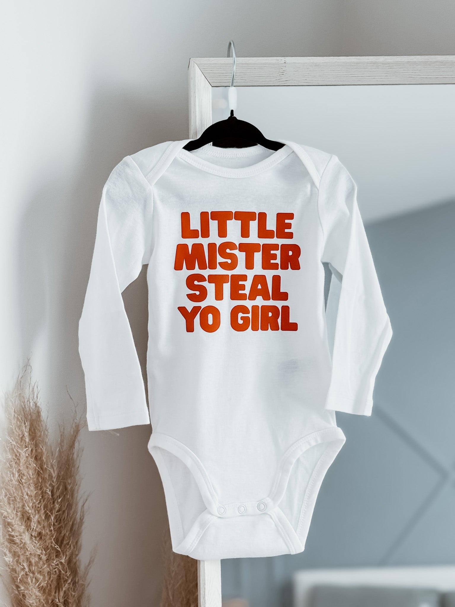 White baby onesie with red text on a hanger against a neutral background