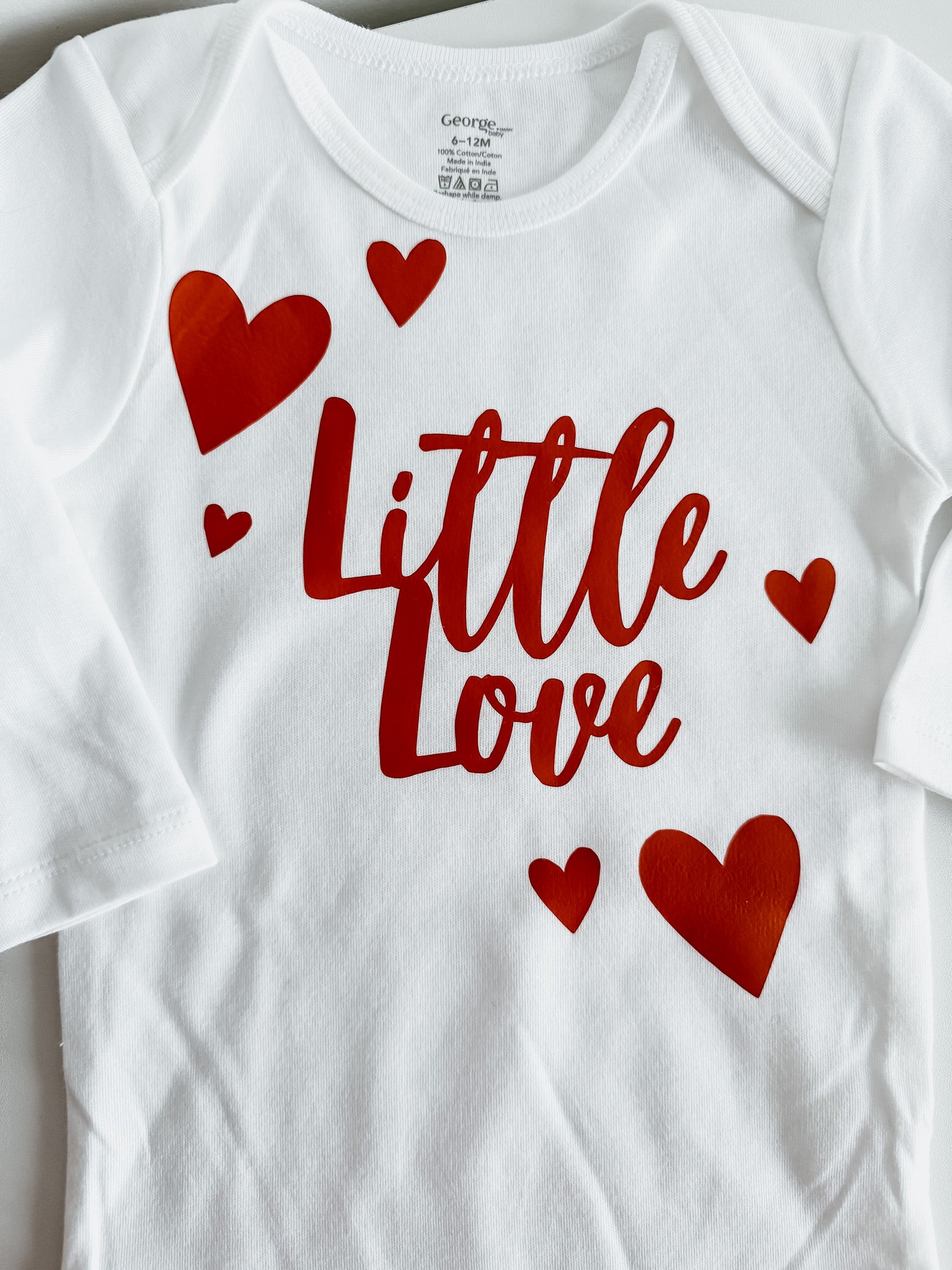 White baby onesie with red 'Little Love' text and hearts on a white background