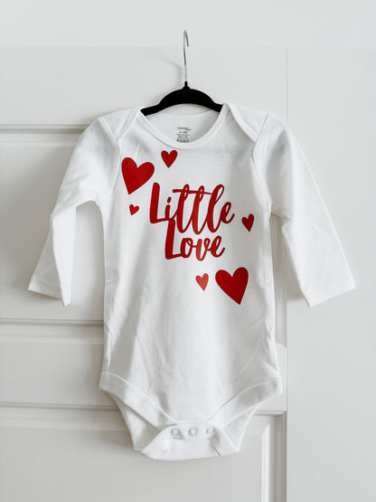 White baby onesie with red text and hearts on a hanger against a white background