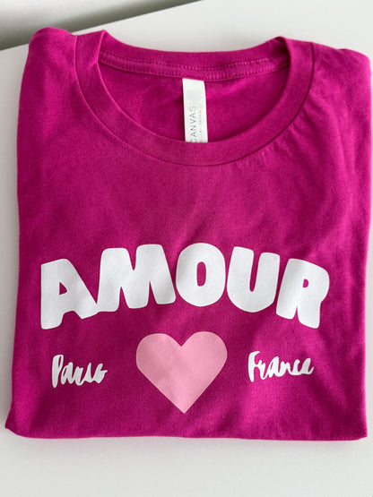 Folded pink t-shirt with 'AMOUR Paris France' text and a heart on a white background
