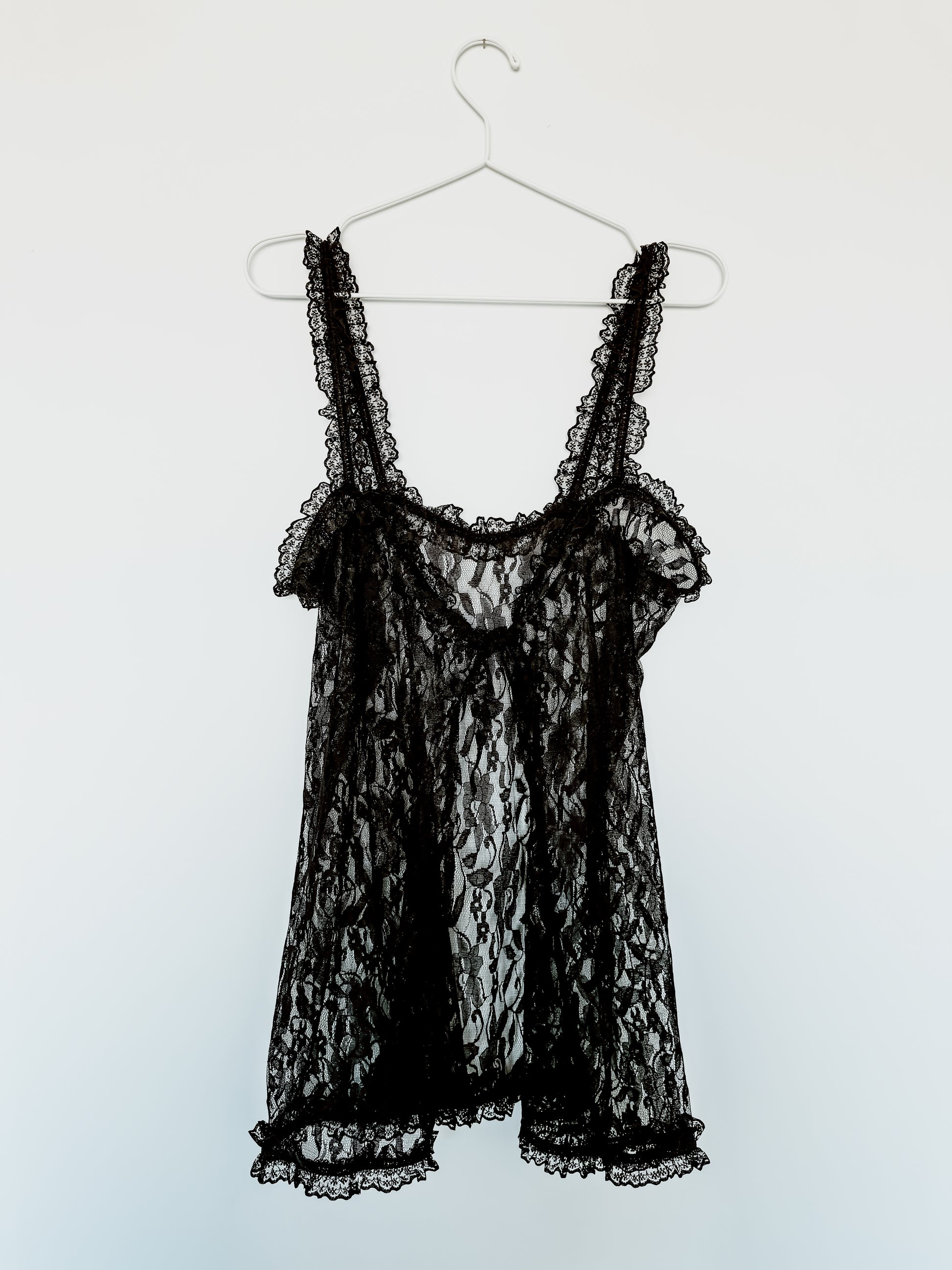 Black lace babydoll dress on a hanger against a white background